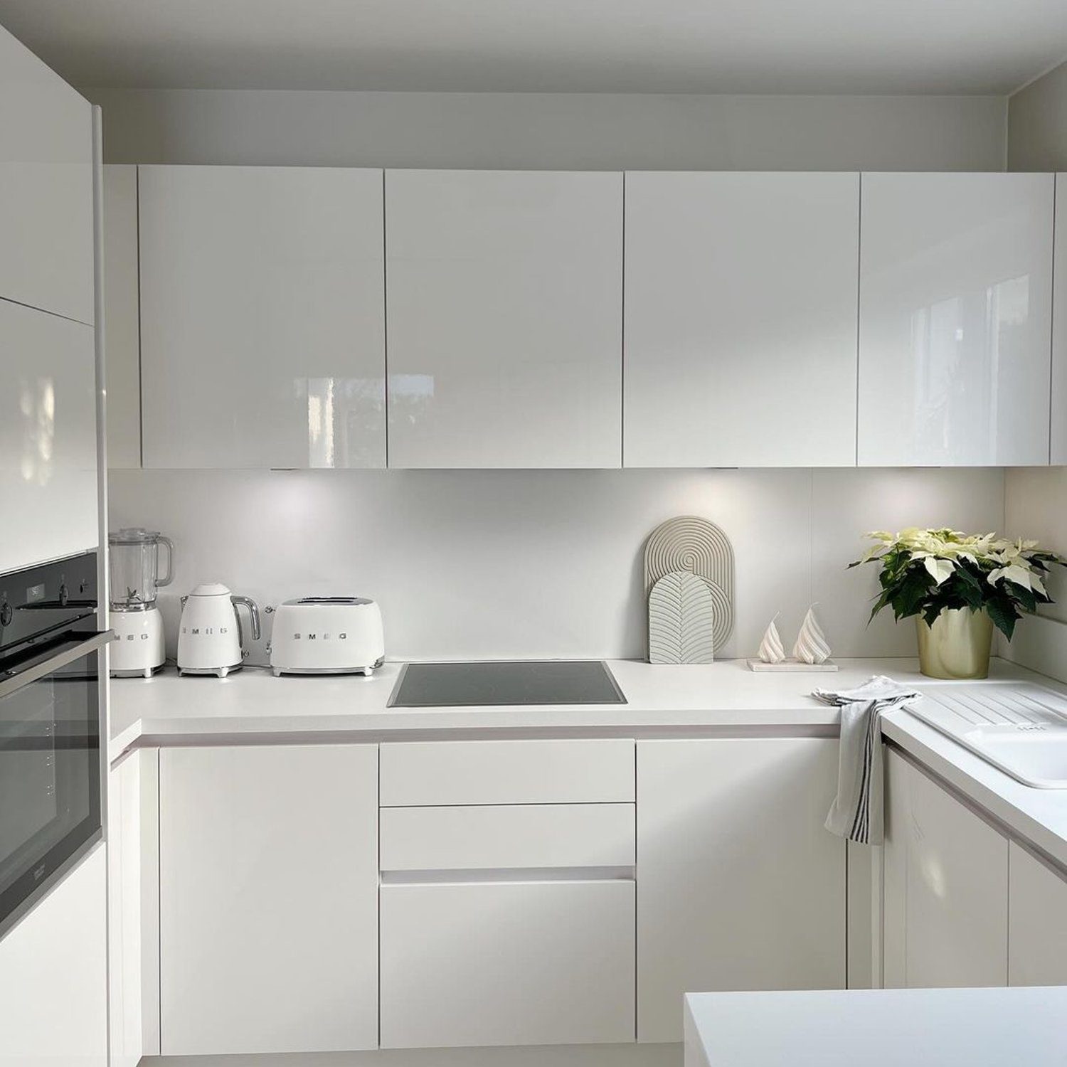 A minimalist kitchen with gleaming white cabinets, modern appliances, and a wooden floor.