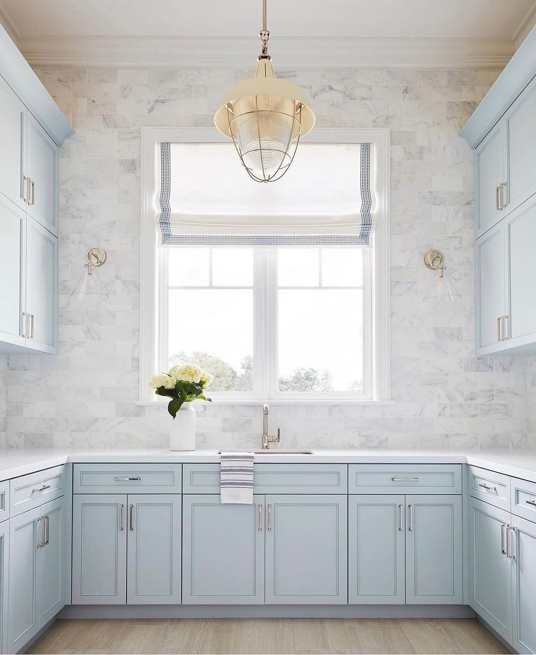 A serene kitchen design featuring soft blue cabinetry, marble backsplash, and brass accents