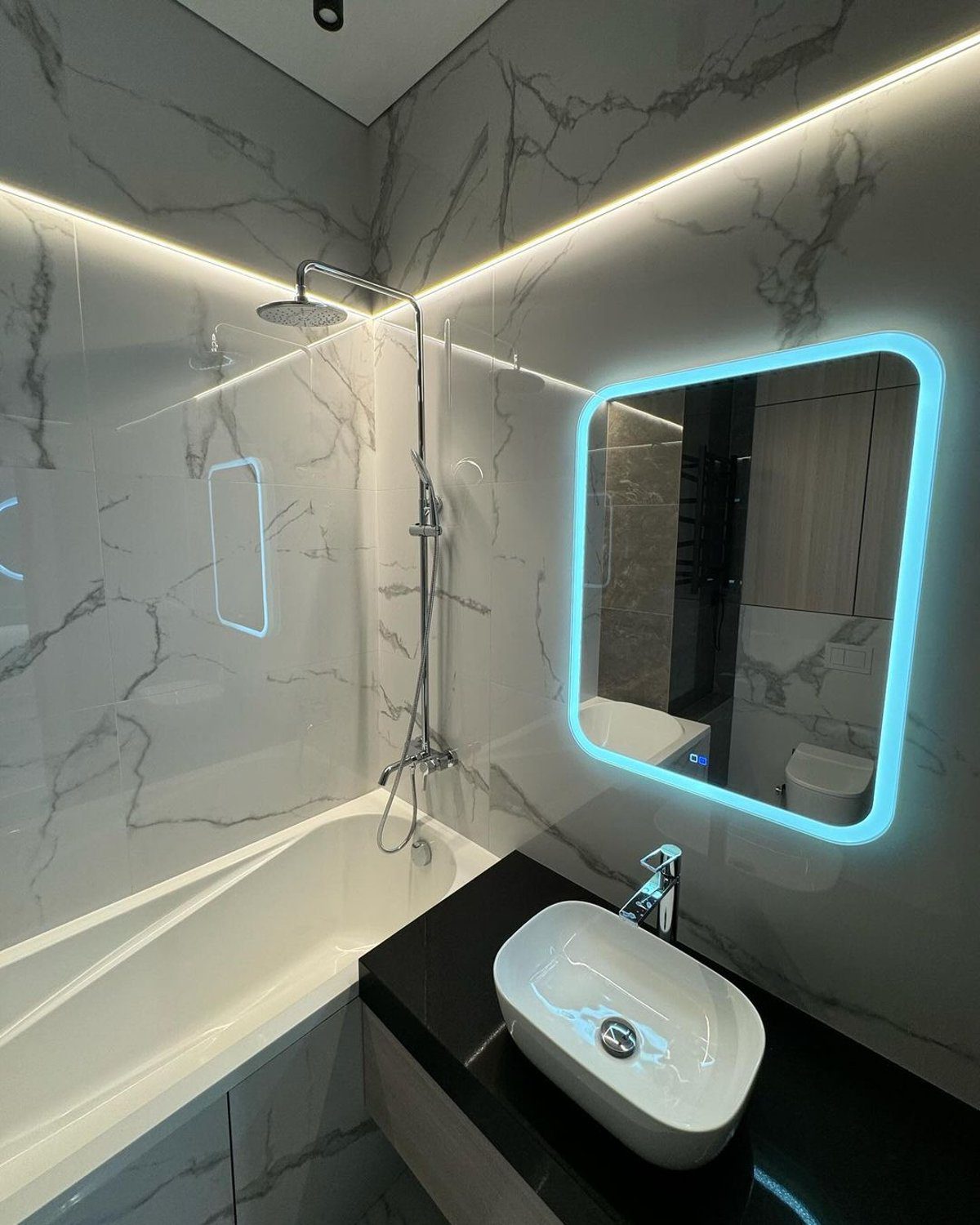 A chic modern bathroom featuring marbled tile walls, sleek backlit mirror, and contrasting dark fixtures for a touch of elegance.