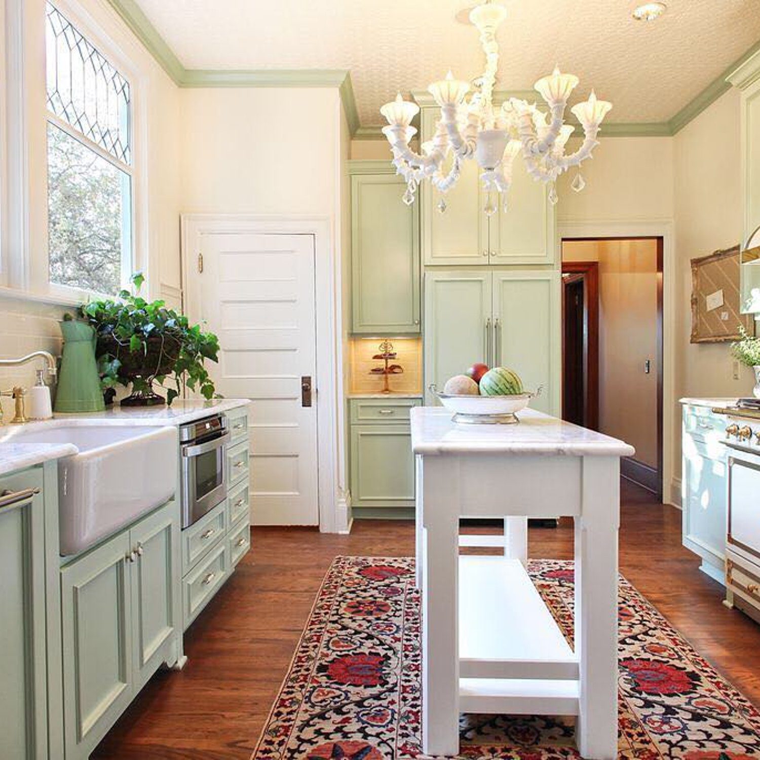 Elegant vintage-inspired kitchen featuring pastel green cabinetry, an ornate white chandelier, and a vibrant area rug