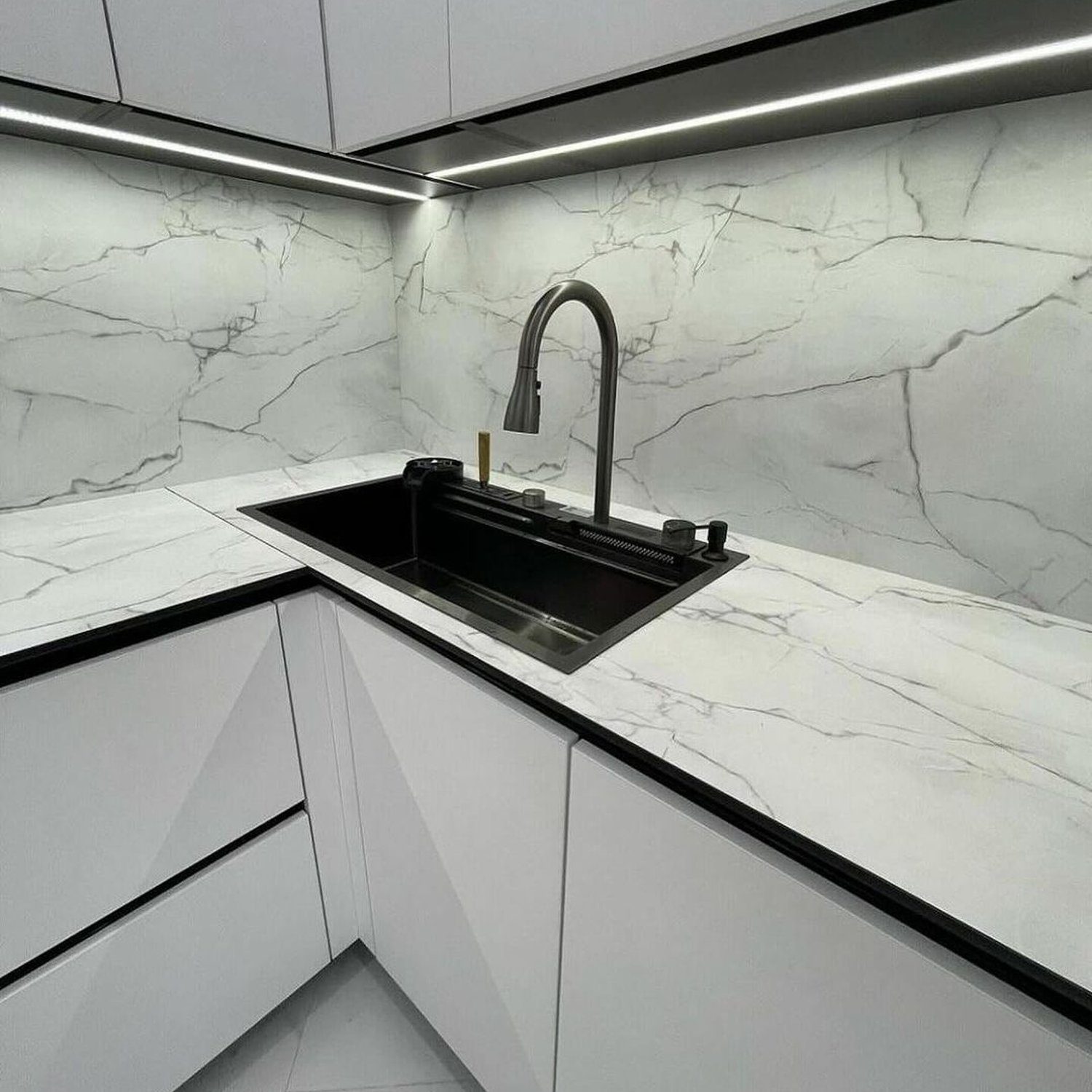 A sleek and modern kitchen design featuring marbled walls and countertops, with an black undermount sink and a stainless steel faucet.