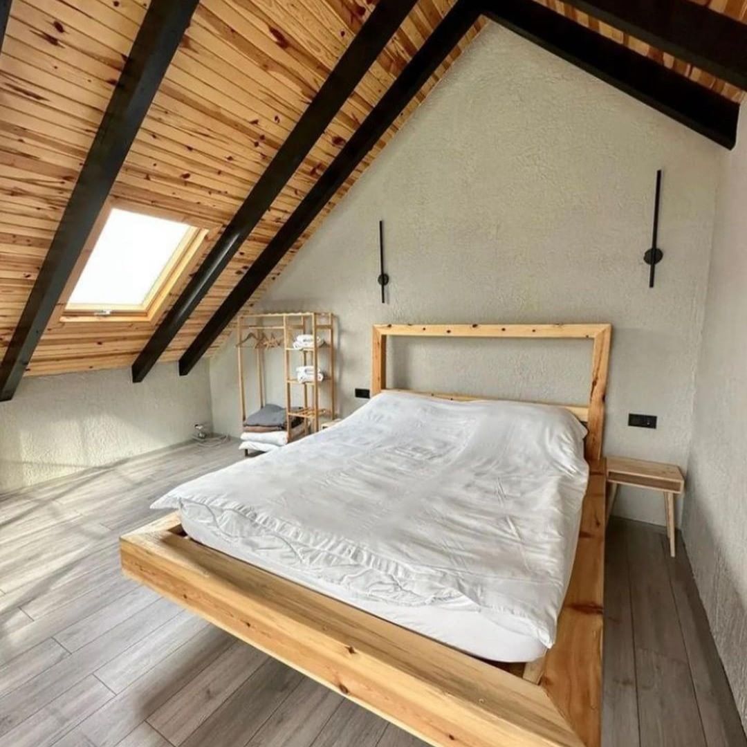 A cozy attic bedroom showcasing exposed wooden beams on the ceiling and a skylight