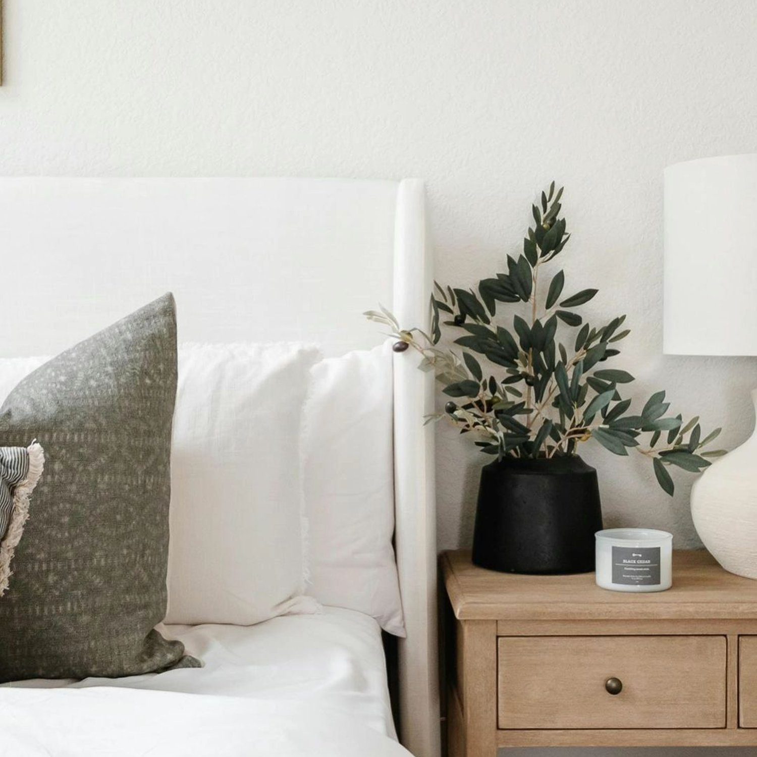 A neatly organized bedroom corner featuring a white bed with grey and white pillow accents