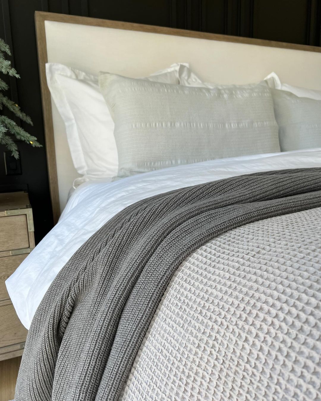 A neatly made bed with textured grey blankets and pillows