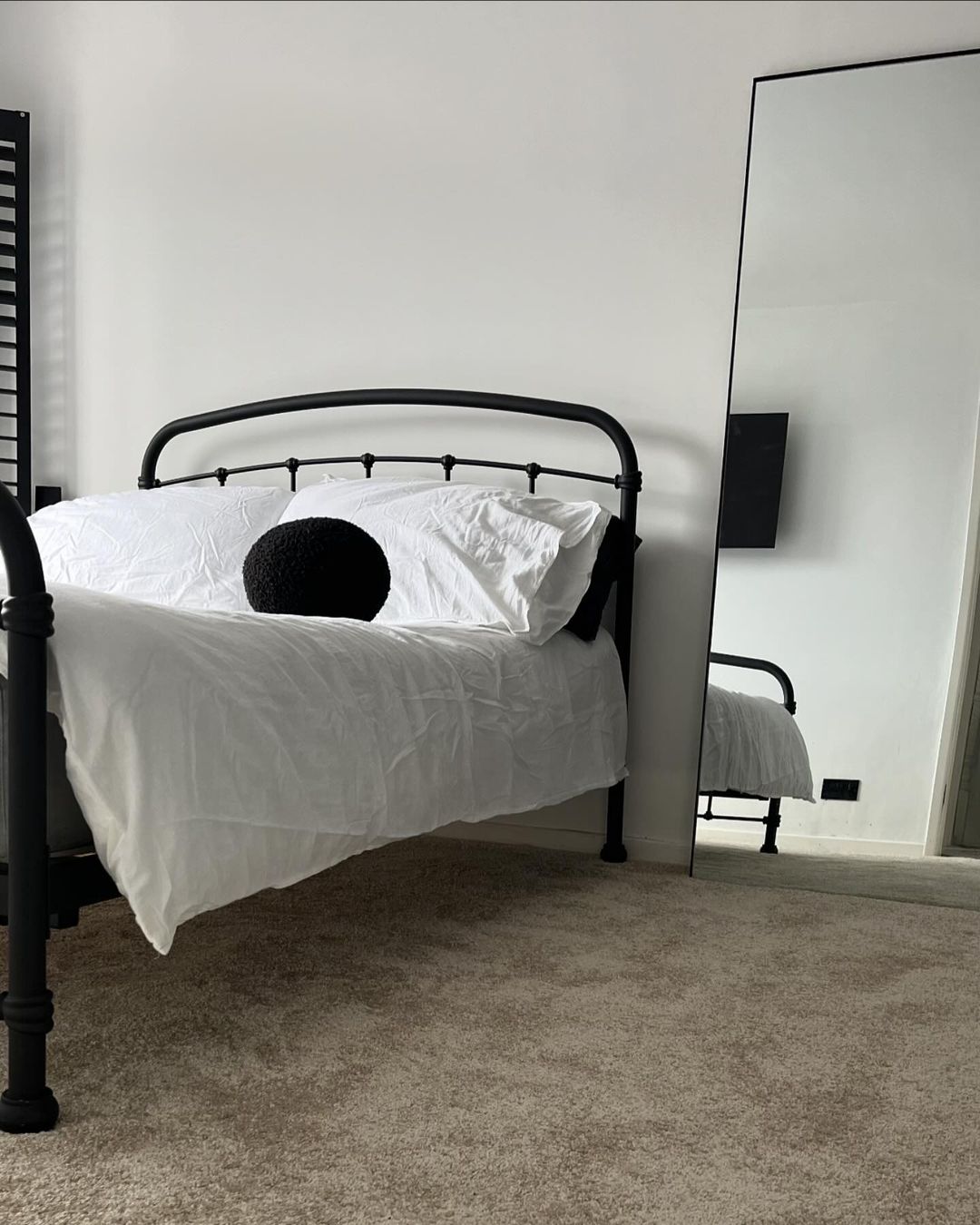 A neatly made bed with a black headboard, white bedding, and a single dark pillow resting at the center.