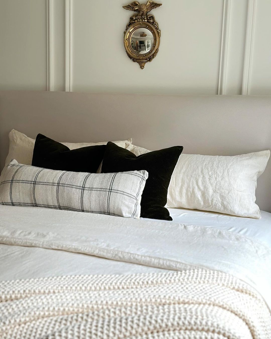 A neatly arranged bed with a decorative mirror above