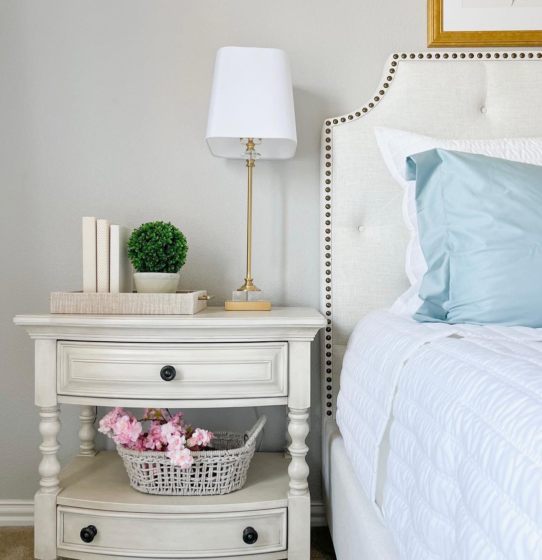 A neatly-arranged bedside scene with a lamp, books, and flower basket.