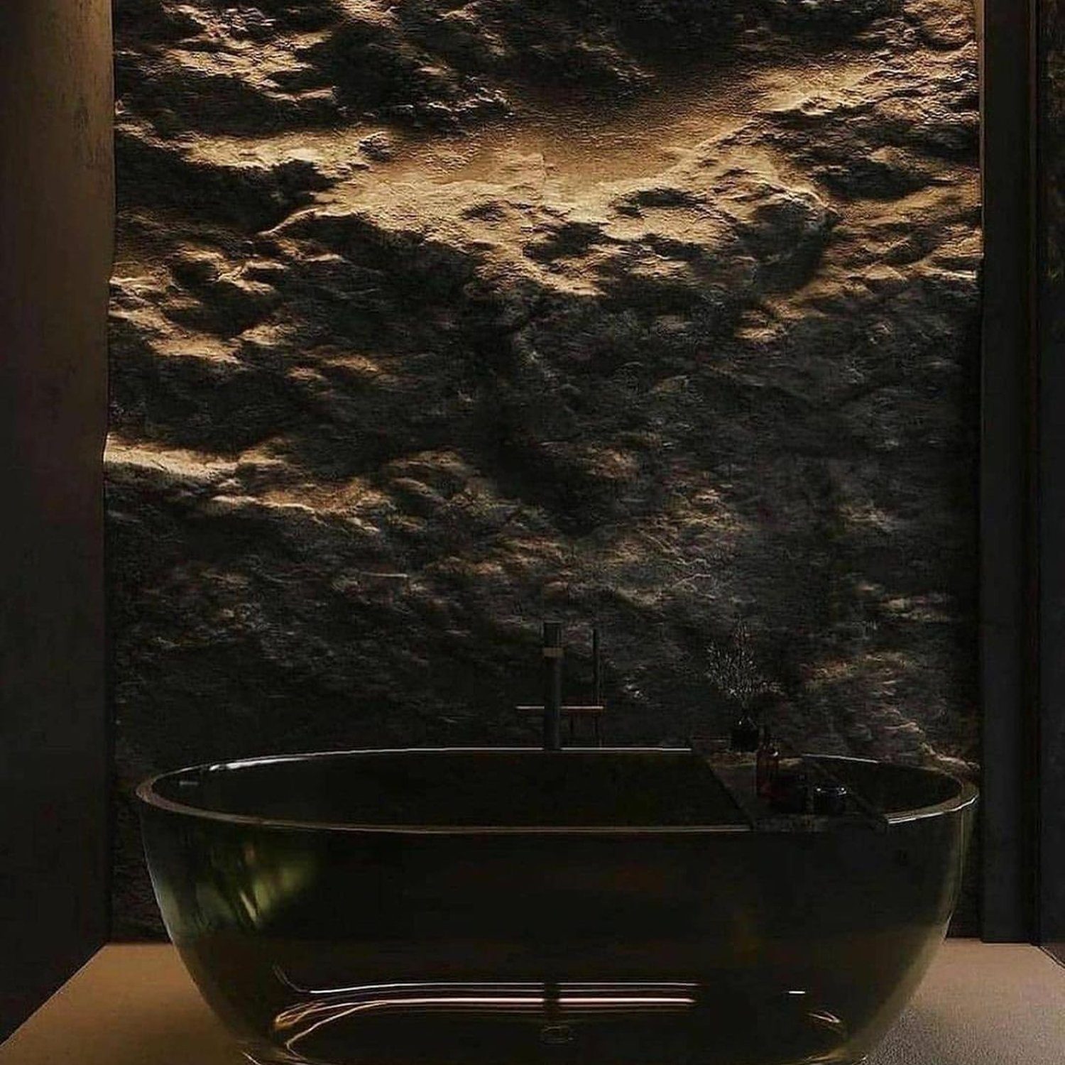 Sleek black freestanding bathtub against a textured stone wall with warm accent lighting