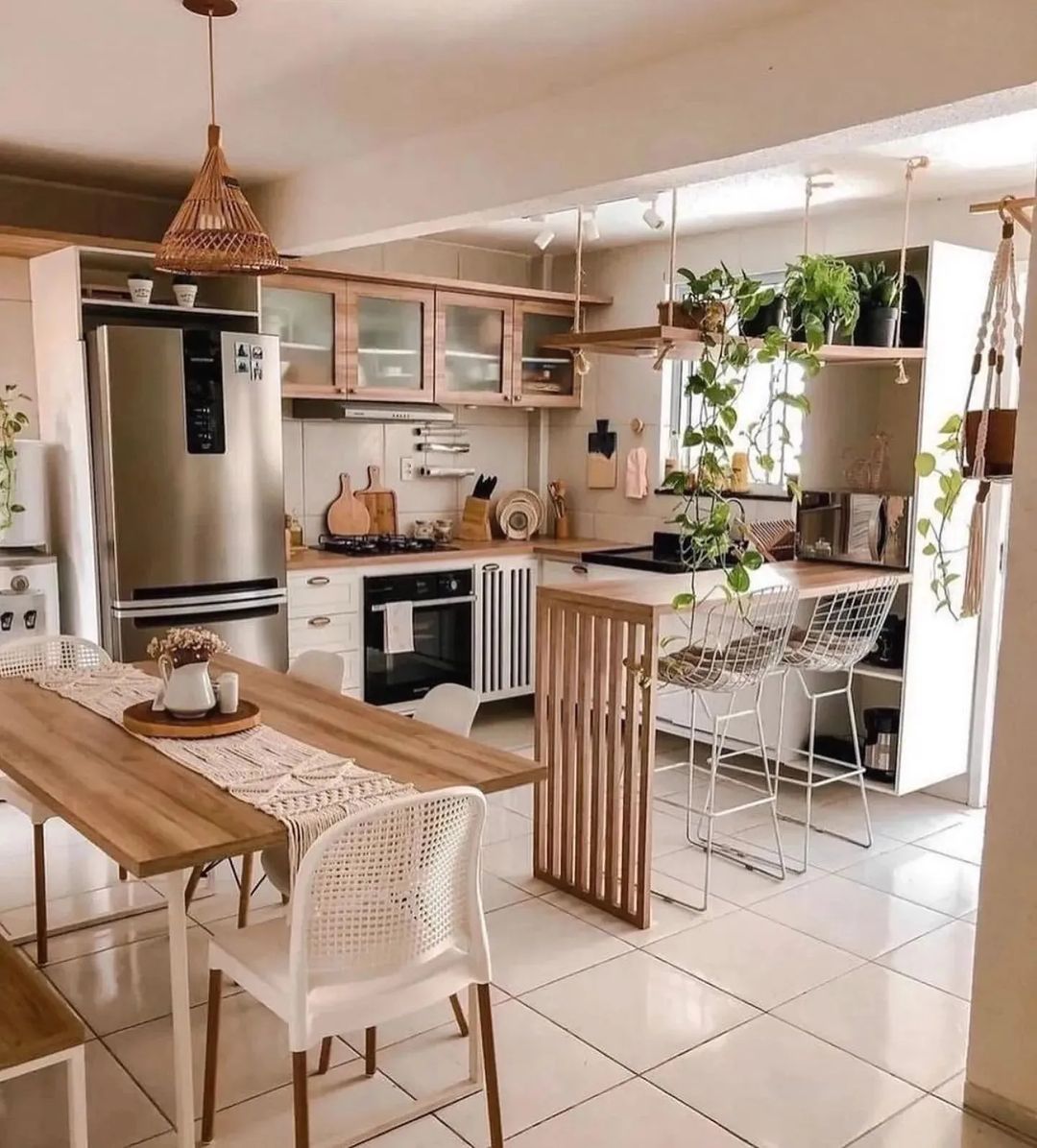 A harmonious blend of natural materials and modern design in a kitchen featuring wooden cabinetry, a sleek, stainless steel refrigerator, suspended greenery, and a cozy dining area.