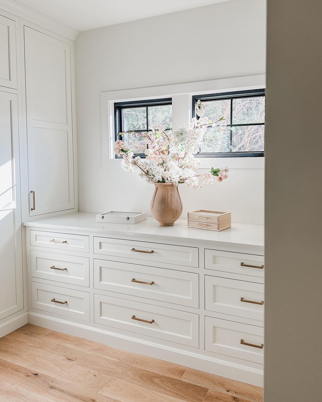 A minimalist interior with white cabinetry and gold handles, showcasing an earth-toned vase with spring blossoms on a cabinet.