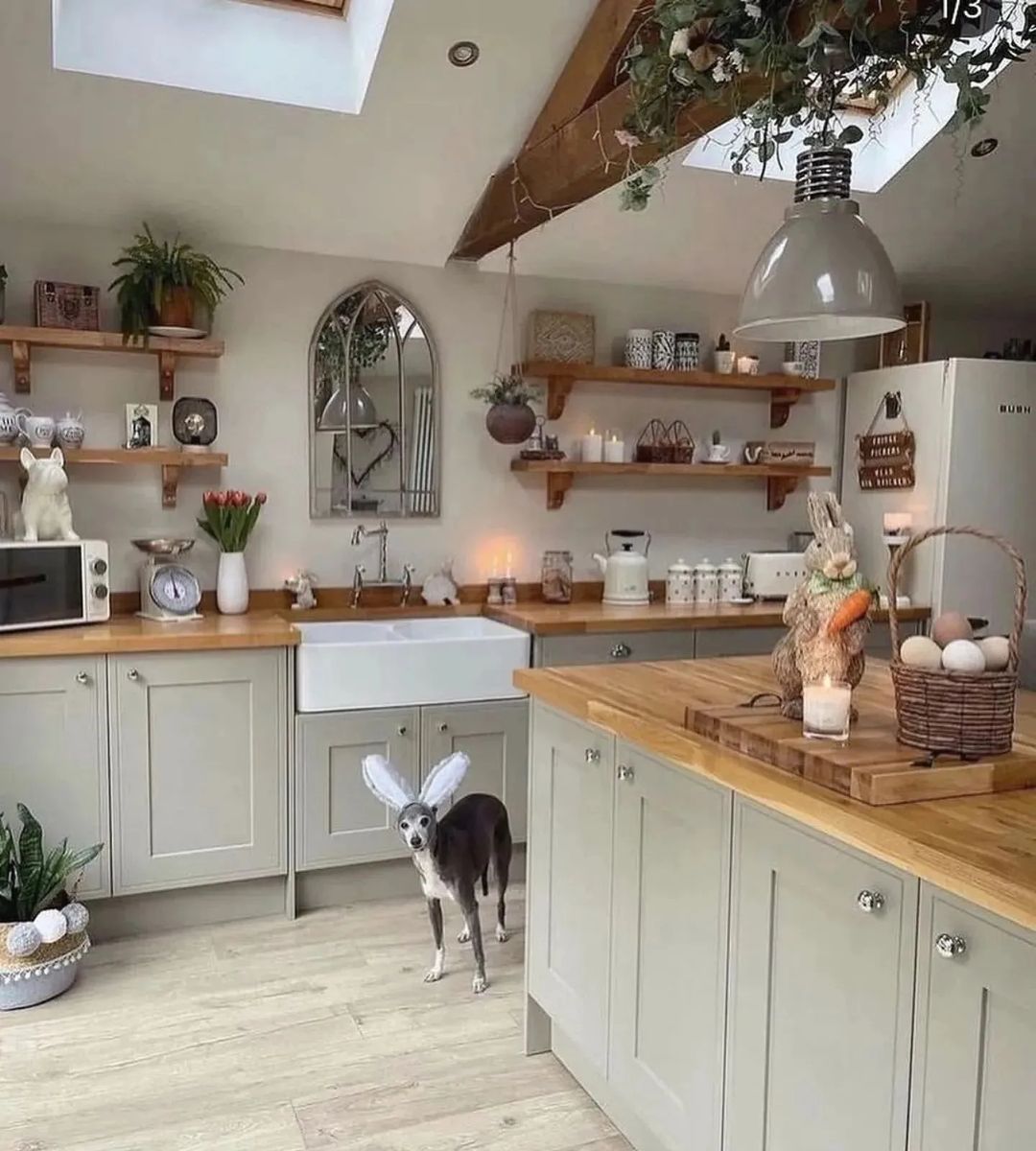 A whimsically adorned dog with faux wings standing in a cozy kitchen featuring open shelving, an arched mirror, and rustic accents.