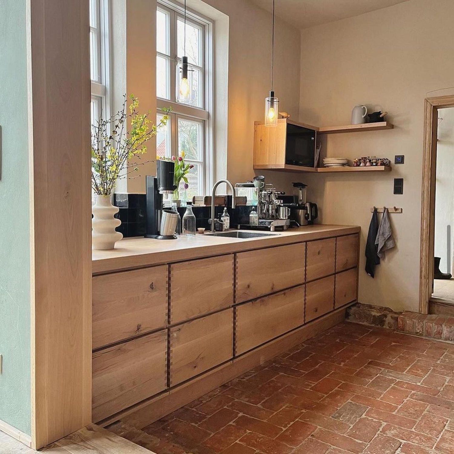 A rustic yet modern kitchen with warm terracotta floor tiles and a sleek wooden counter featuring an array of espresso machines