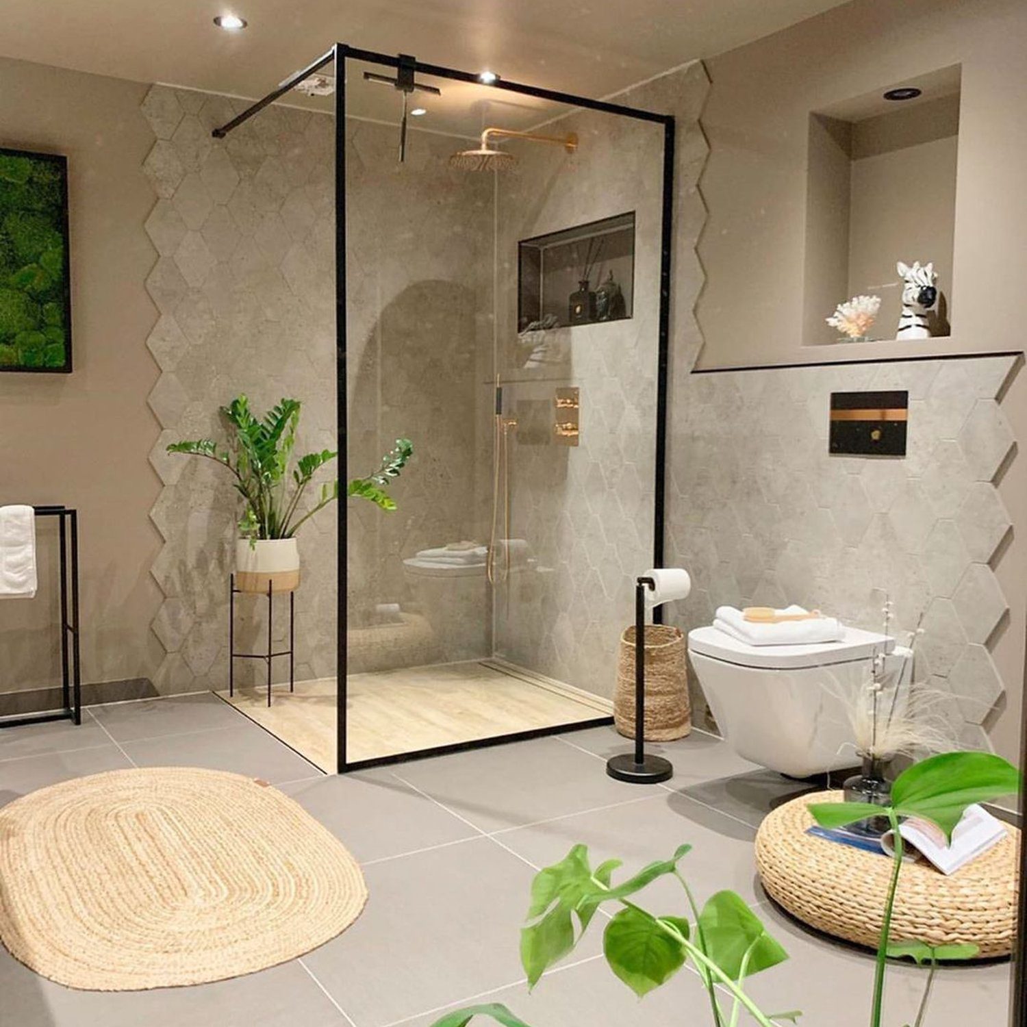 A chic and elegant bathroom featuring textured grey tiles, a glass-enclosed shower, and pops of greenery