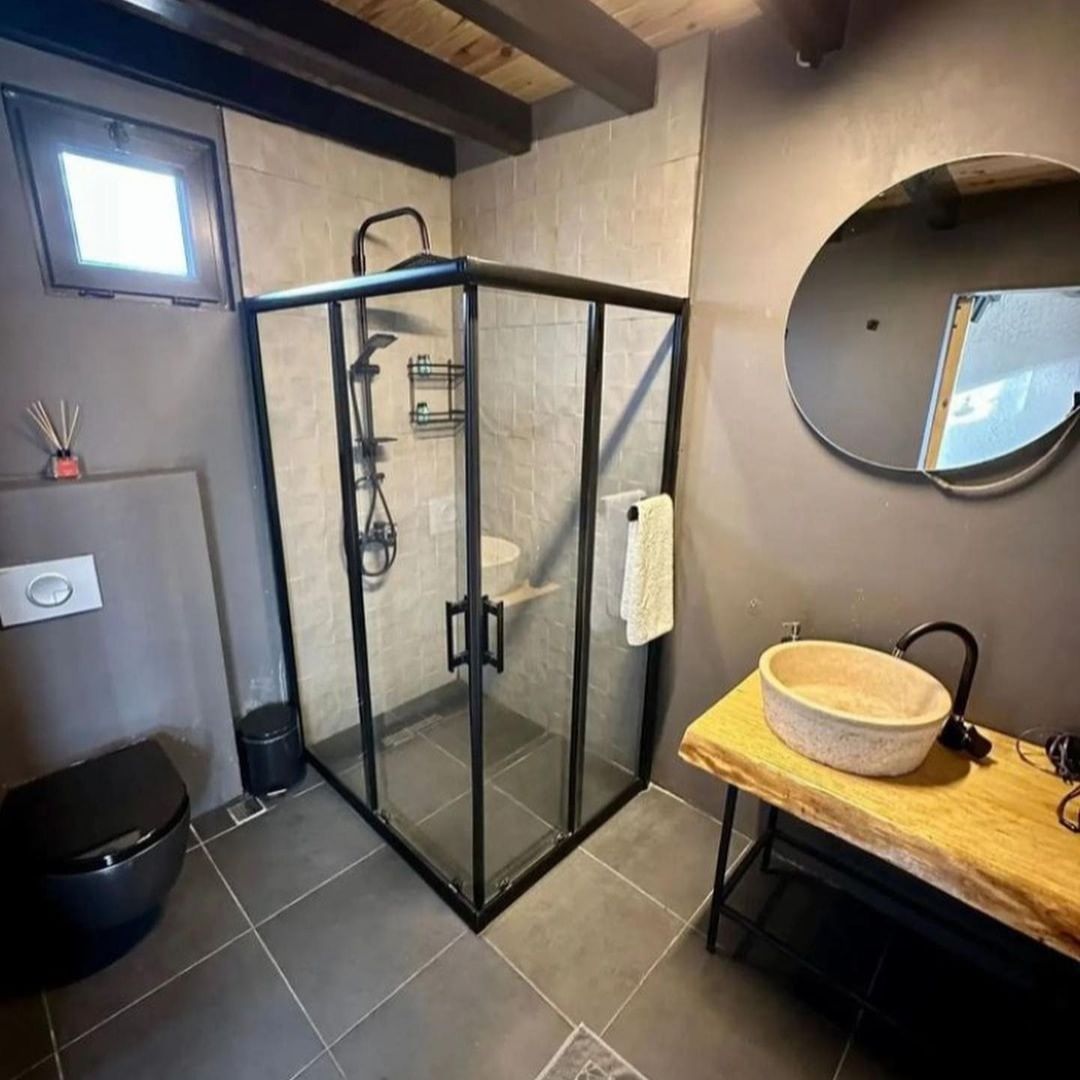 A sleek and modern bathroom featuring grey tiling, a combination of wood and metal for the vanity, a unique stone sink, and a round mirror that enhances the space.