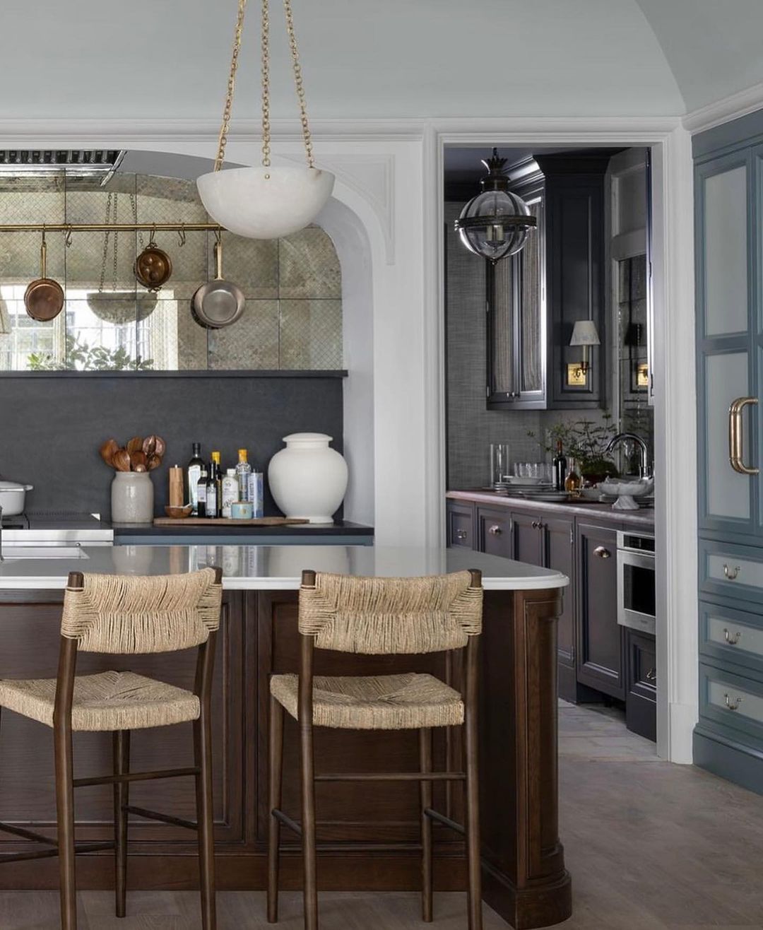 A chic and modern kitchen featuring a blend of dark wood and soft blue cabinetry, with wicker bar stools at a central island