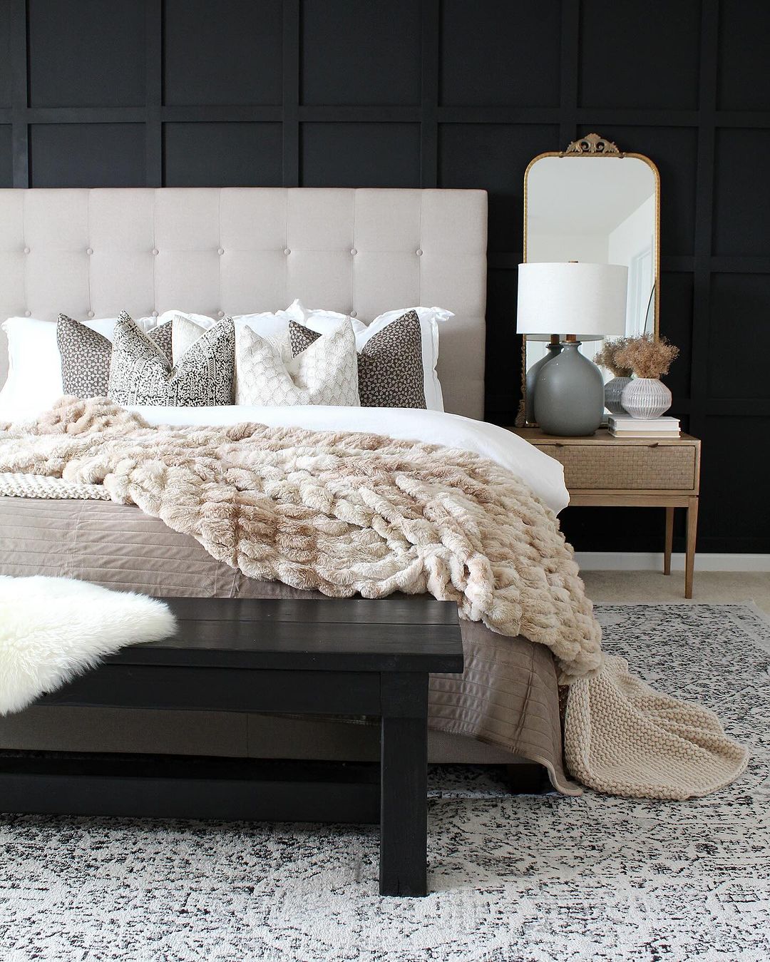 A harmoniously designed bedroom featuring a tufted beige headboard against a bold black paneled wall, complemented by a textured throw blanket and patterned pillows