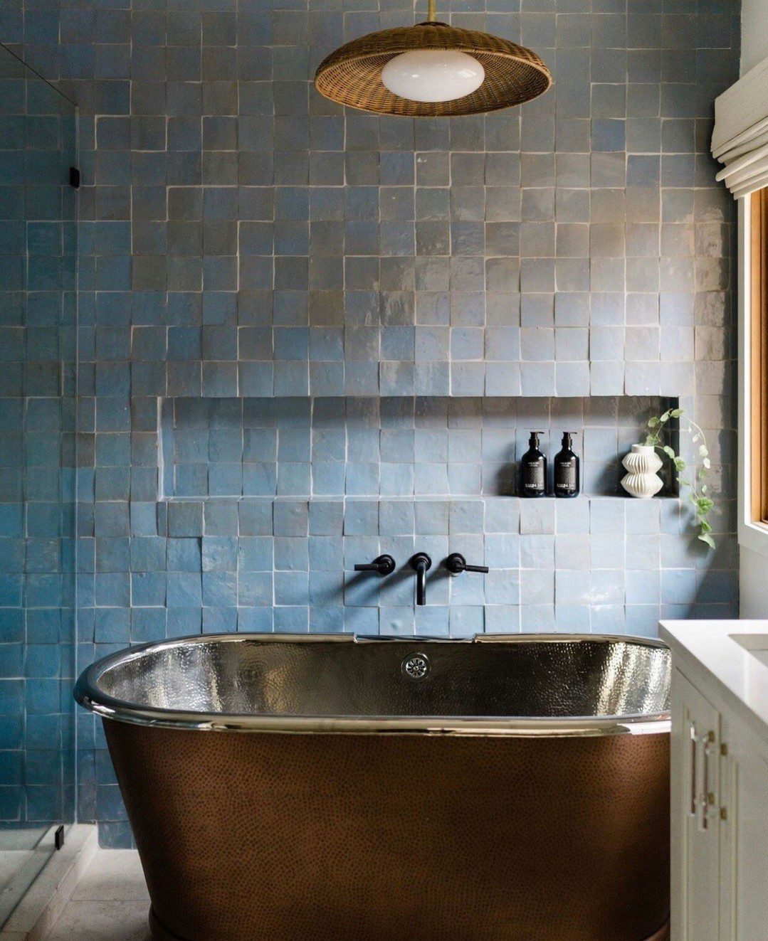 A chic blue-tiled bathroom featuring a copper freestanding tub