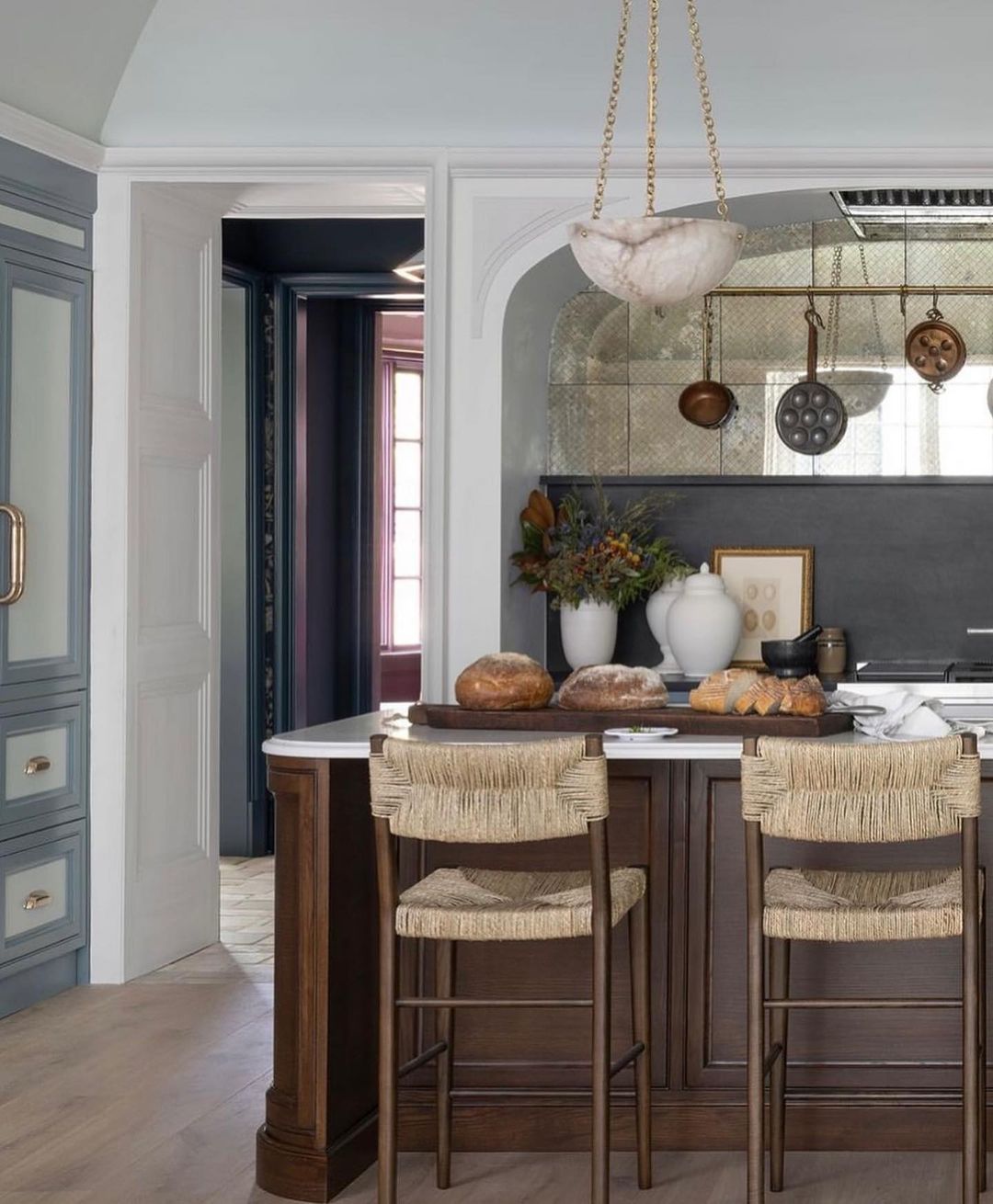 A chic kitchen featuring blue cabinetry, woven bar stools, and hanging copper cookware.