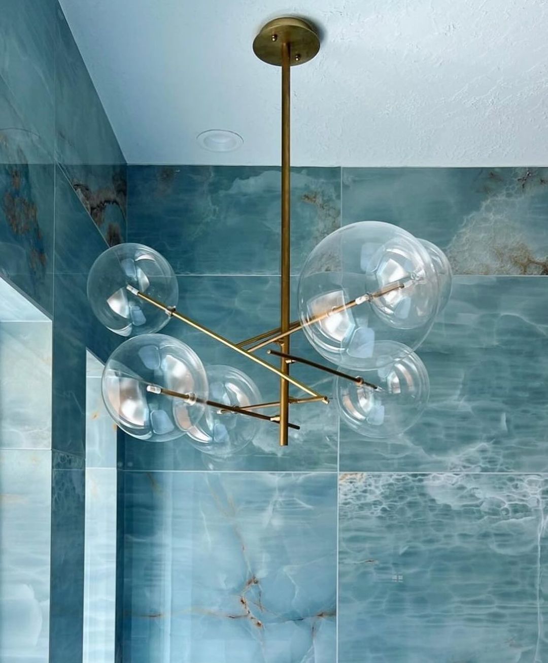 A contemporary bathroom featuring blue marble walls and a unique spherical glass chandelier with brass details