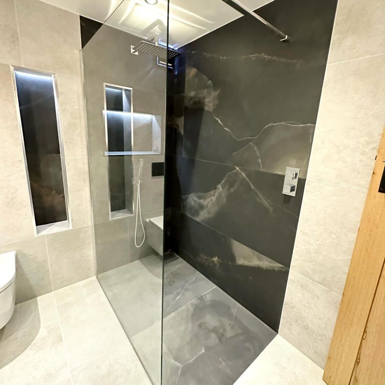 A modern and sleek bathroom featuring a corner glass shower, marble-like tiles, and a minimalist design