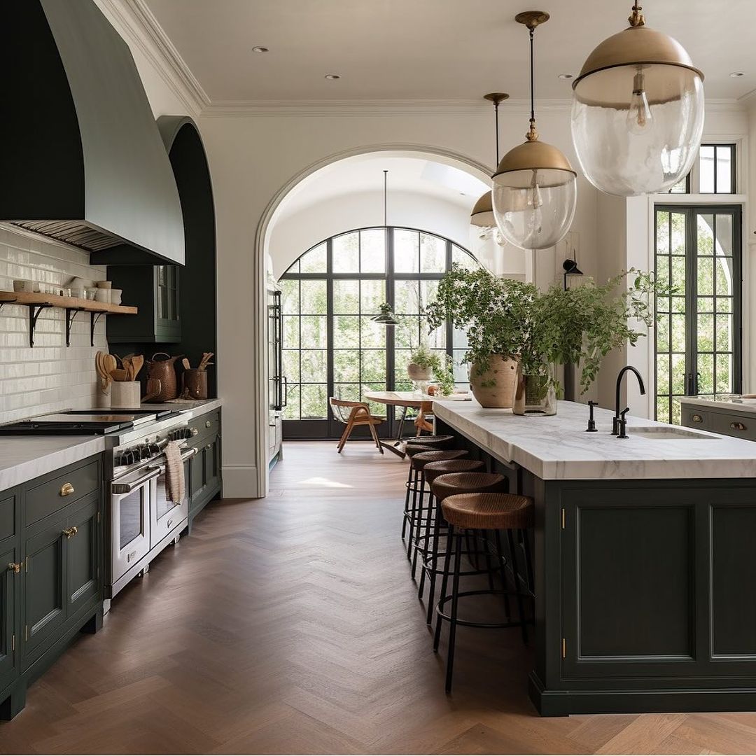 A sophisticated kitchen featuring dark green cabinetry, marble countertops, and chevron wood flooring