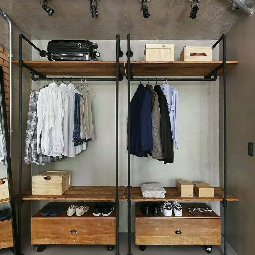 A chic and modern walk-in closet with industrial piping for hangers and wooden elements