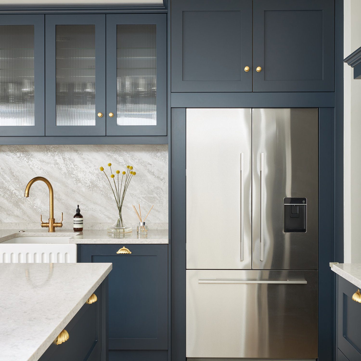 A chic navy blue kitchen featuring brass accents, herringbone wood floors, and marble backsplash