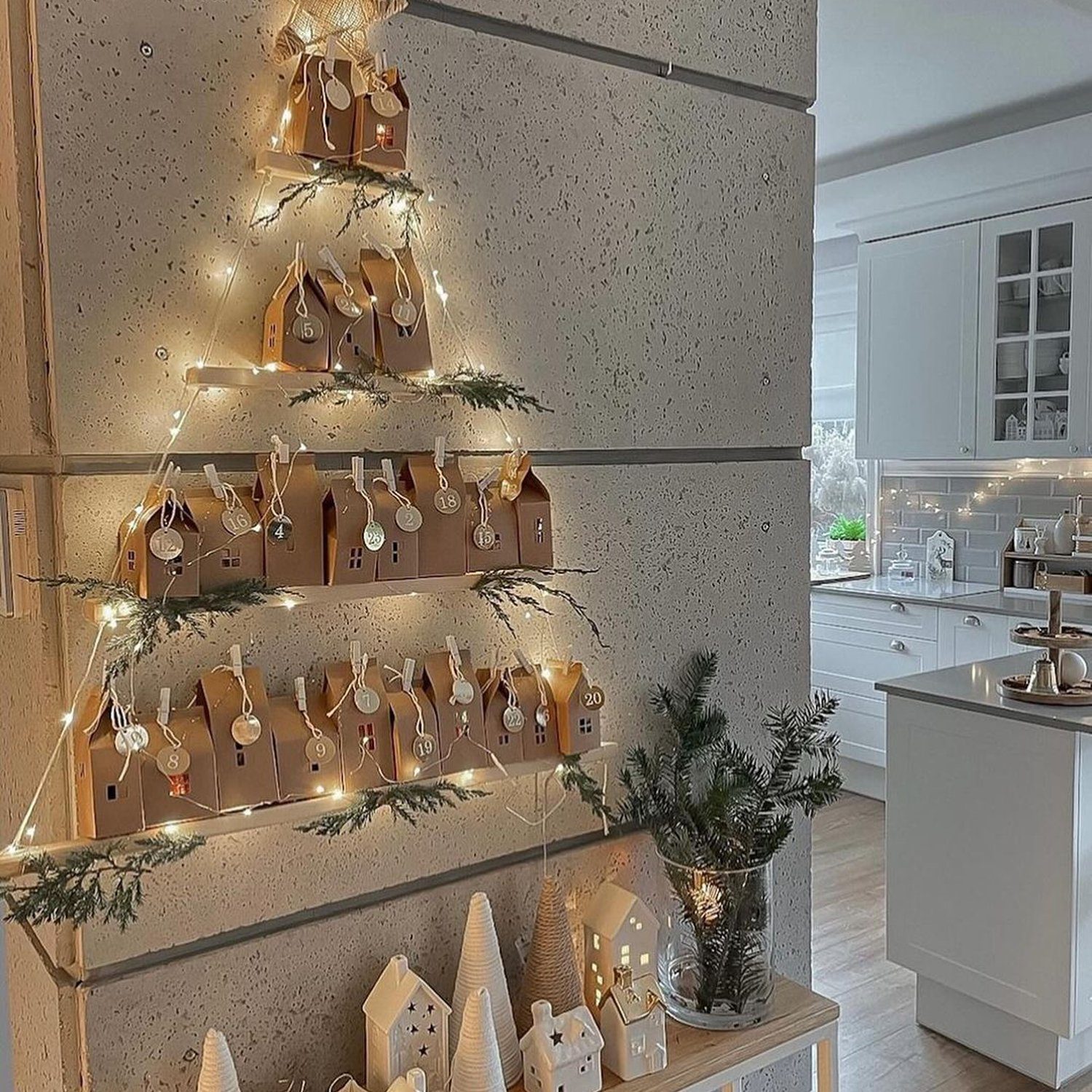 A modern kitchen with a unique Christmas decoration featuring mini houses and string lights arranged in a tree shape on shelving