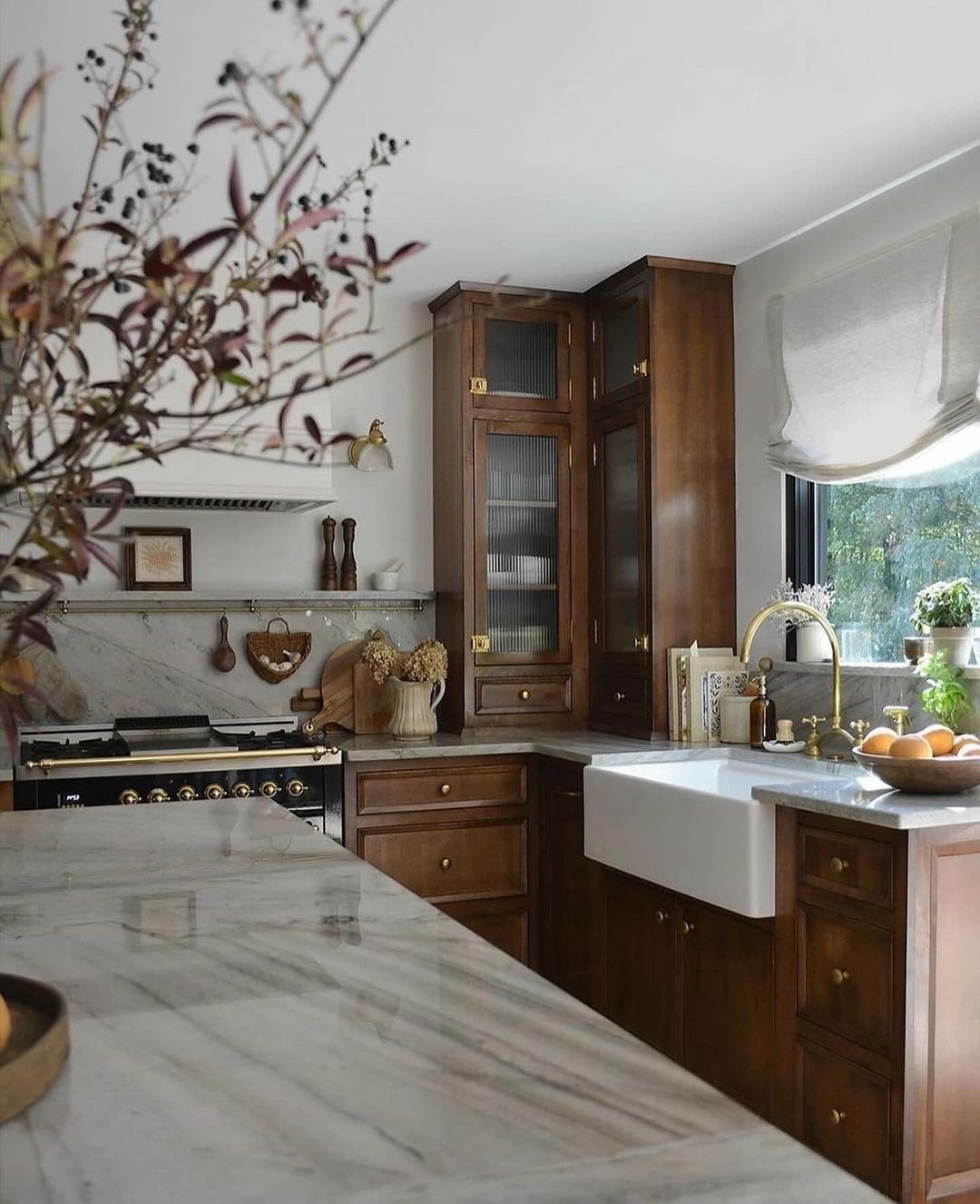 A classic kitchen featuring **rich brown cabinetry** with _gold hardware_, white marble countertops, and a farmhouse-style sink