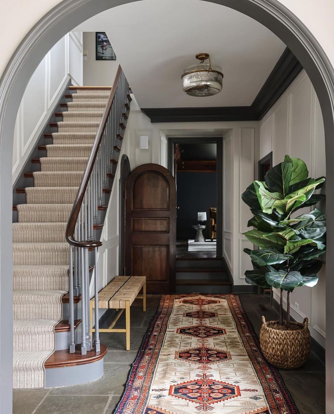 A classic hallway with a curved staircase, patterned runner, and a fiddle leaf fig