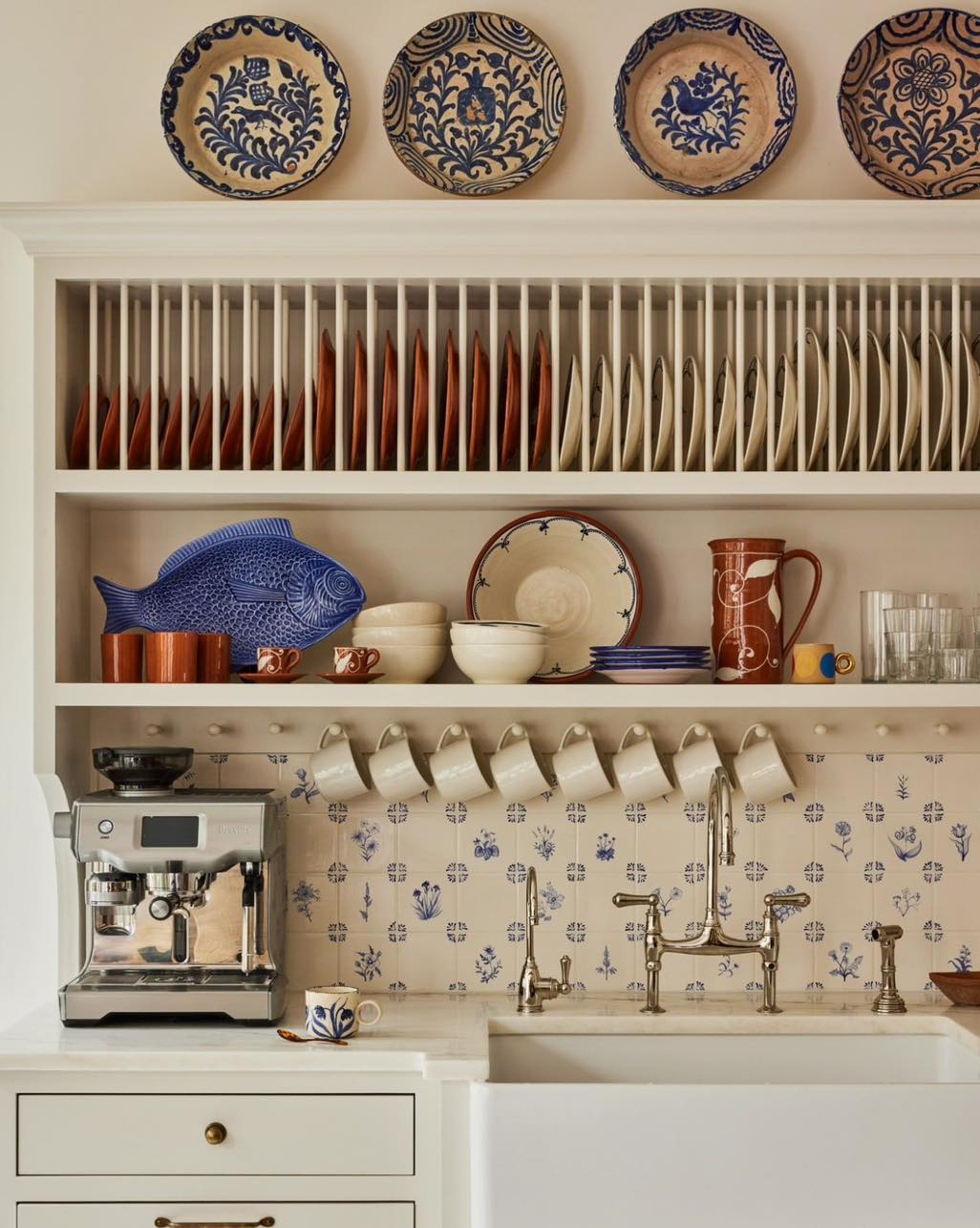 Classic blue and white themed kitchenware displayed above a farmhouse sink with a modern coffee machine, illustrating a harmonious blend of traditional and contemporary elements in a kitchen setting