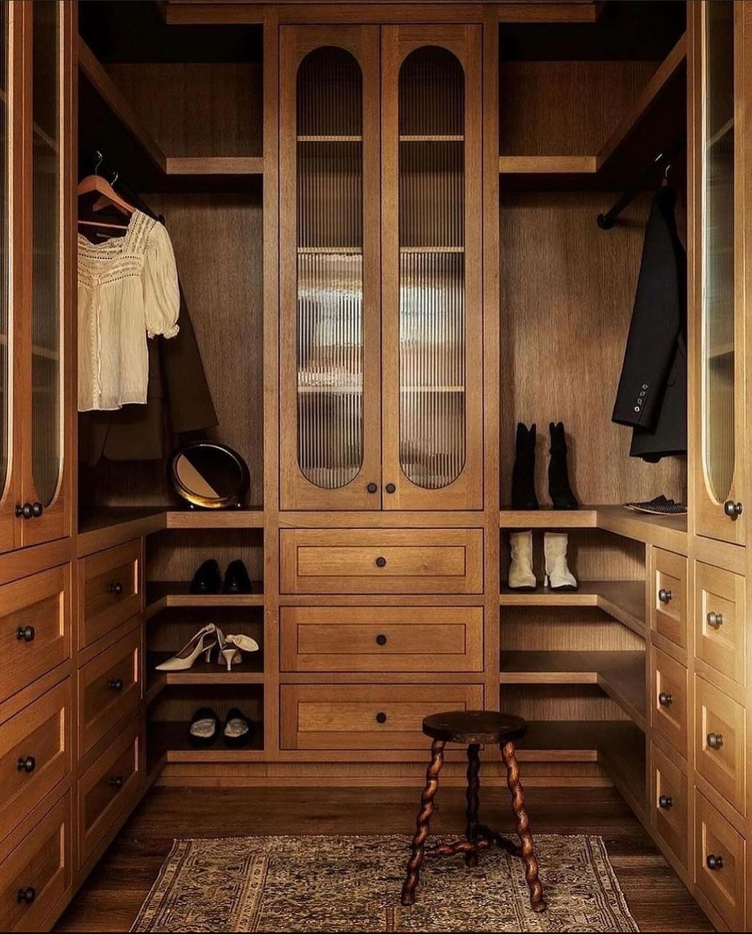 A classy wooden walk-in closet design featuring custom cabinetry and a unique spinning stool.