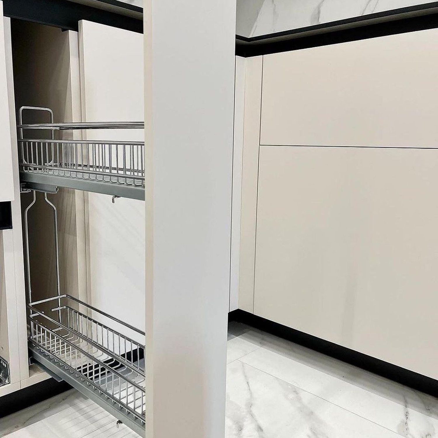 A faultless integration of kitchen cabinetry showcasing an immaculate white pillar ingeniously concealing a sleek, metal pull-out storage system against a backdrop of sumptuous marble-effect tiles.