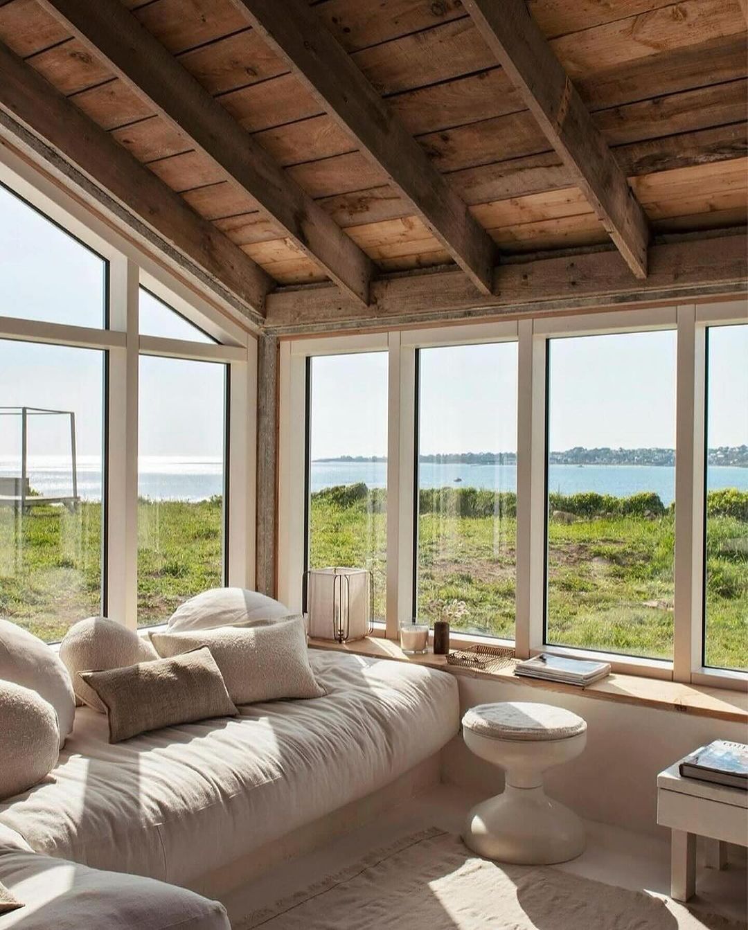 A serene coastal-inspired bedroom with exposed wooden beams and large windows overlooking the sea