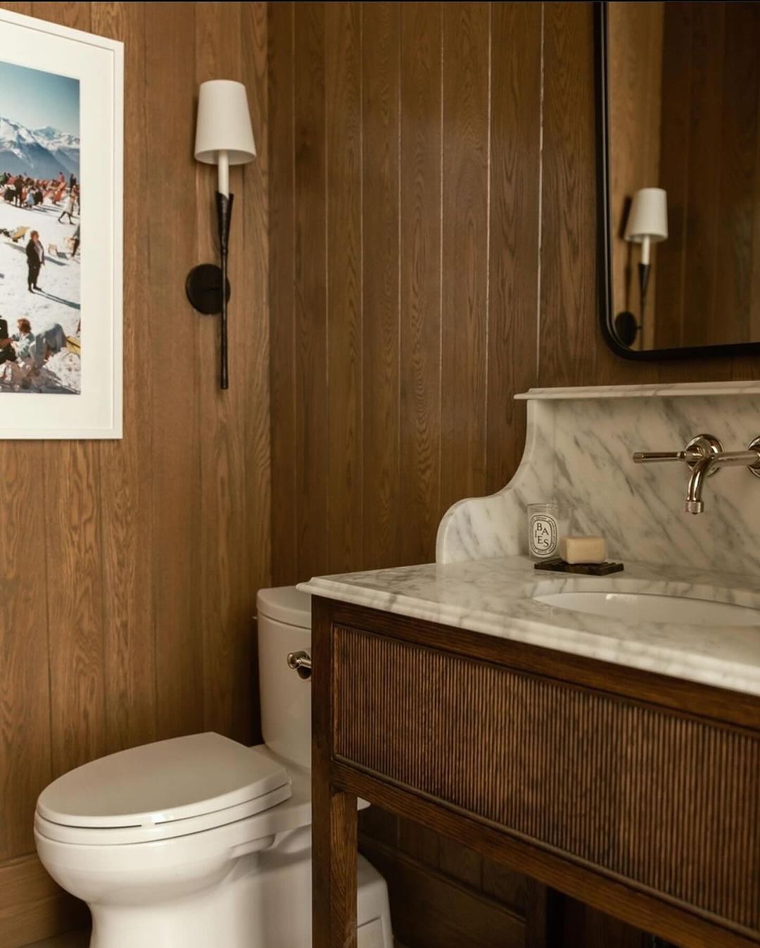 A cozy and inviting bathroom featuring warm wooden panel walls, a chic marble countertop, and modern wall-mounted sconces.