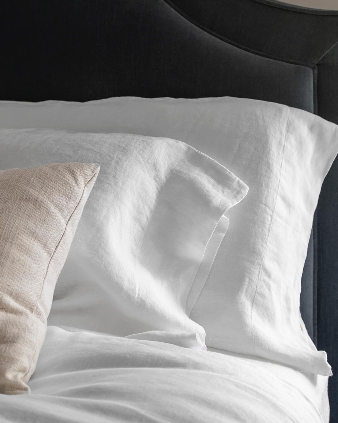 A crisp, white pillow and sheet set on a bed with a dark headboard