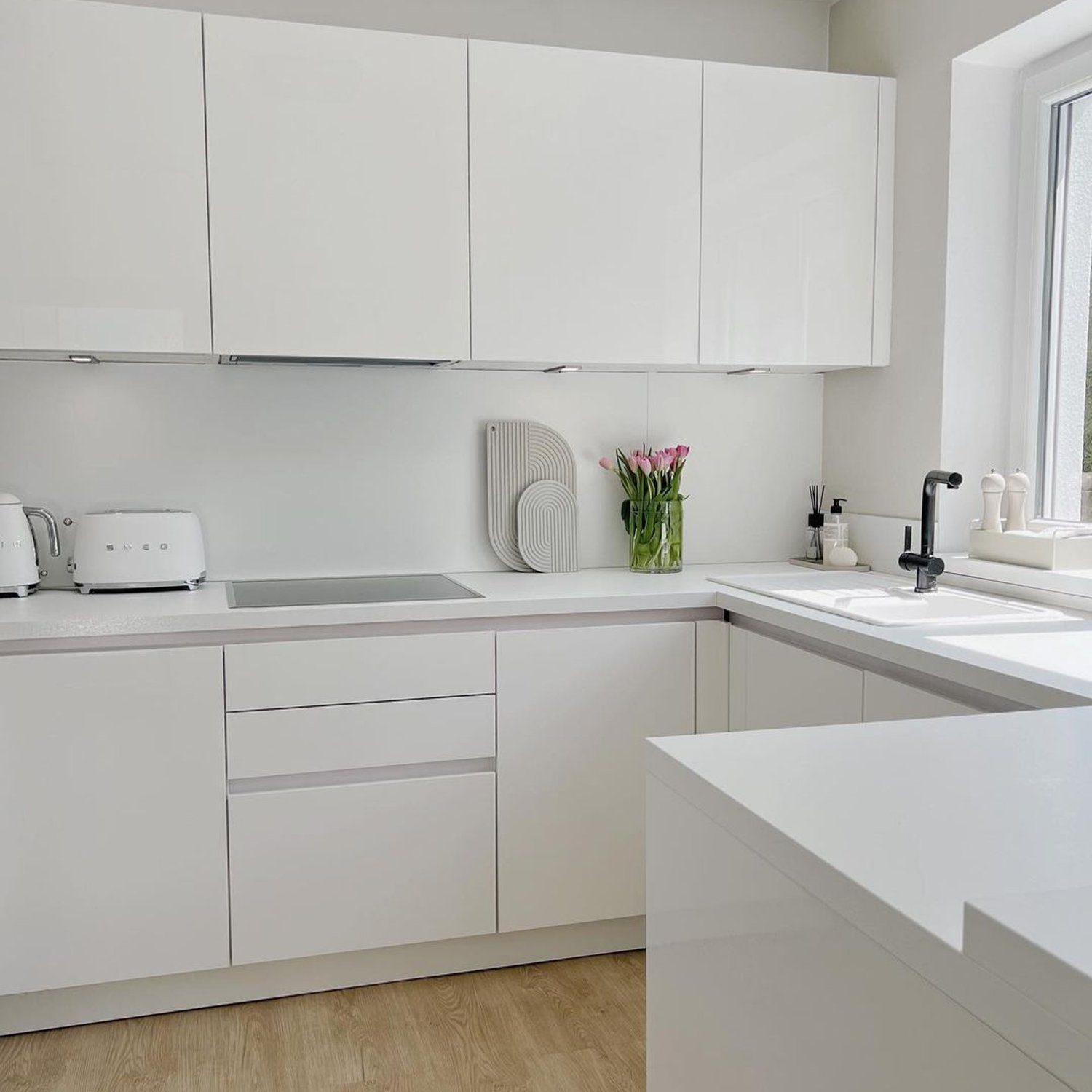 A minimalist kitchen with sleek white cabinetry and wooden flooring