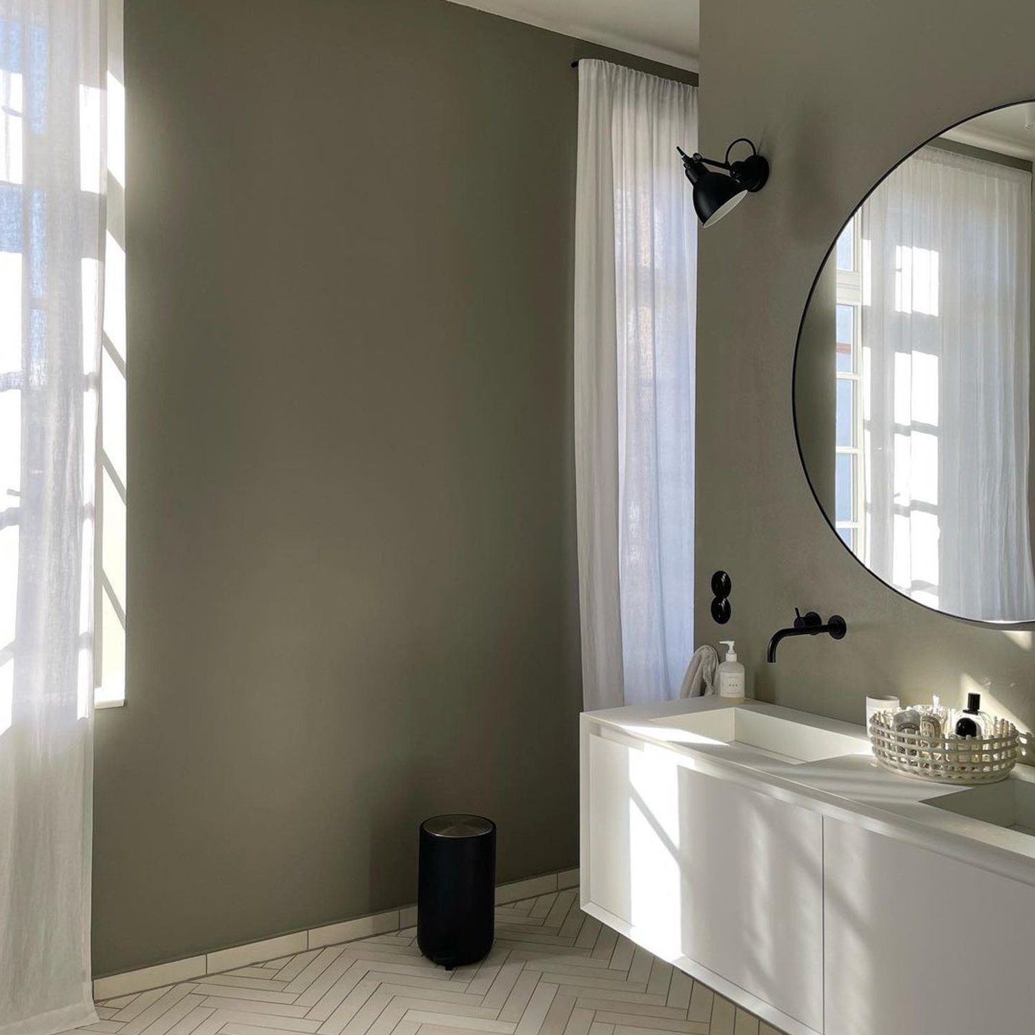 A contemporary bathroom boasting elegance with its matte black fixtures, round mirror, and herringbone tile flooring.