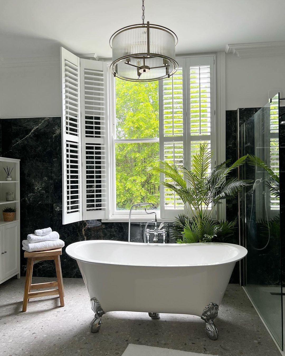 A chic and modern bathroom boasting a freestanding clawfoot tub, black marble walls, and a pristine glass shower enclosure