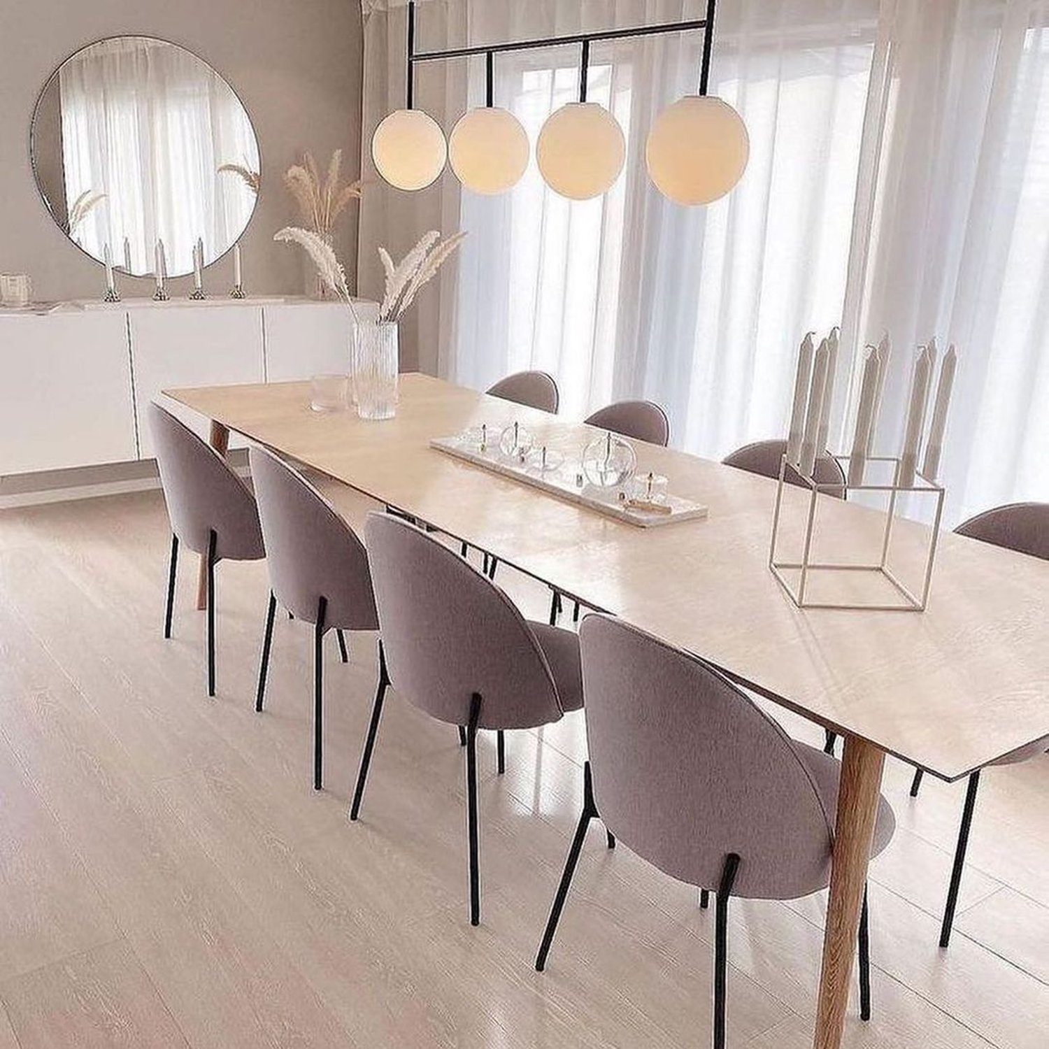 A minimalist dining room featuring a long wooden table, grey upholstered chairs, and a modern pendant light with round opaque globes