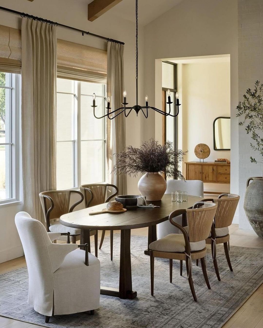 A modern dining room design featuring a dark wooden round table surrounded by mixed styles of chairs