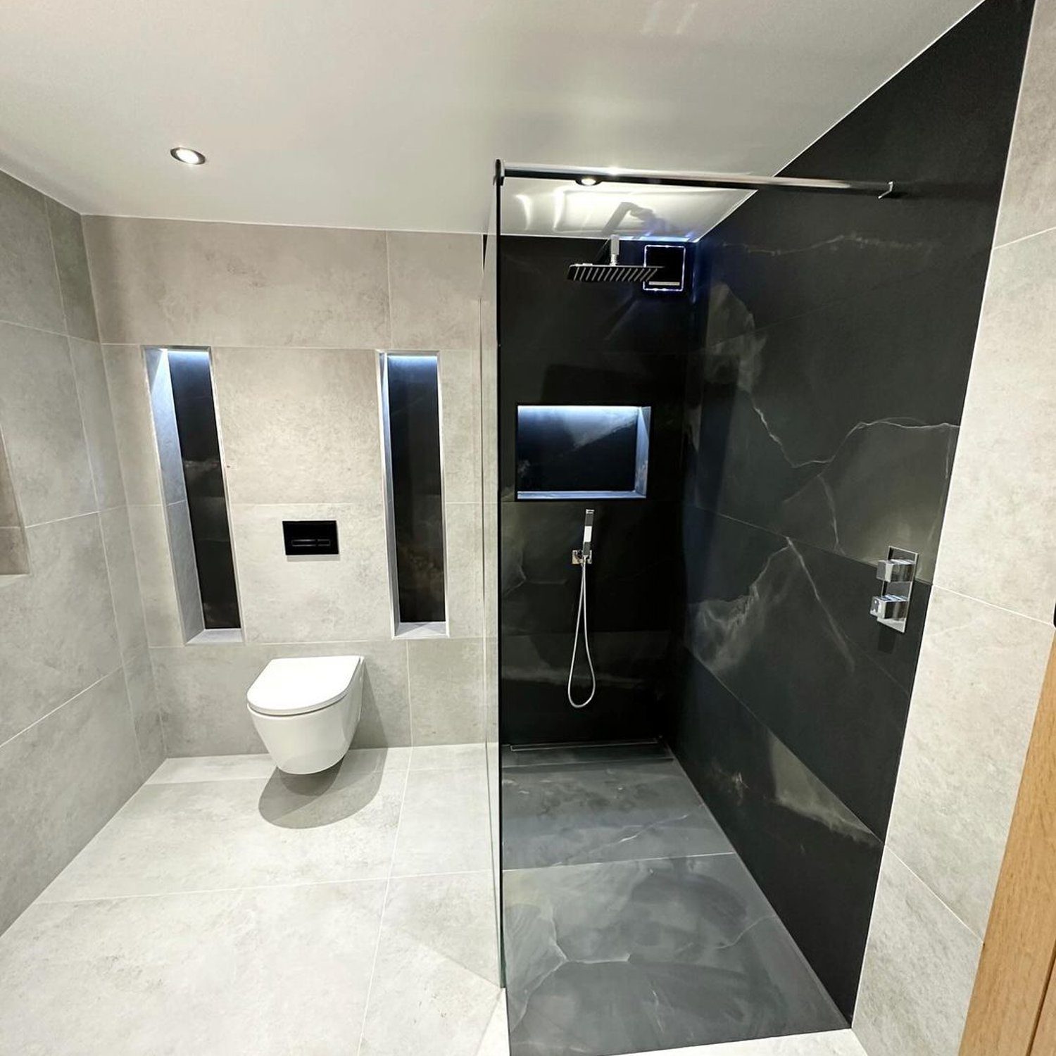 A contemporary bathroom featuring sleek grey tiles, wall-mounted toilet, and a walk-in shower with a black marble accent