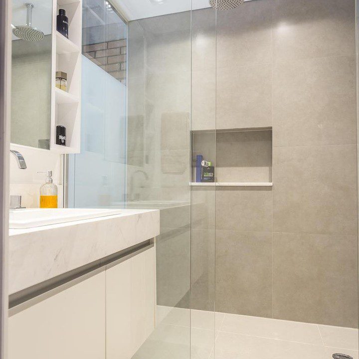 A modern grey tiled bathroom featuring a glass-enclosed shower area and built-in shelving units