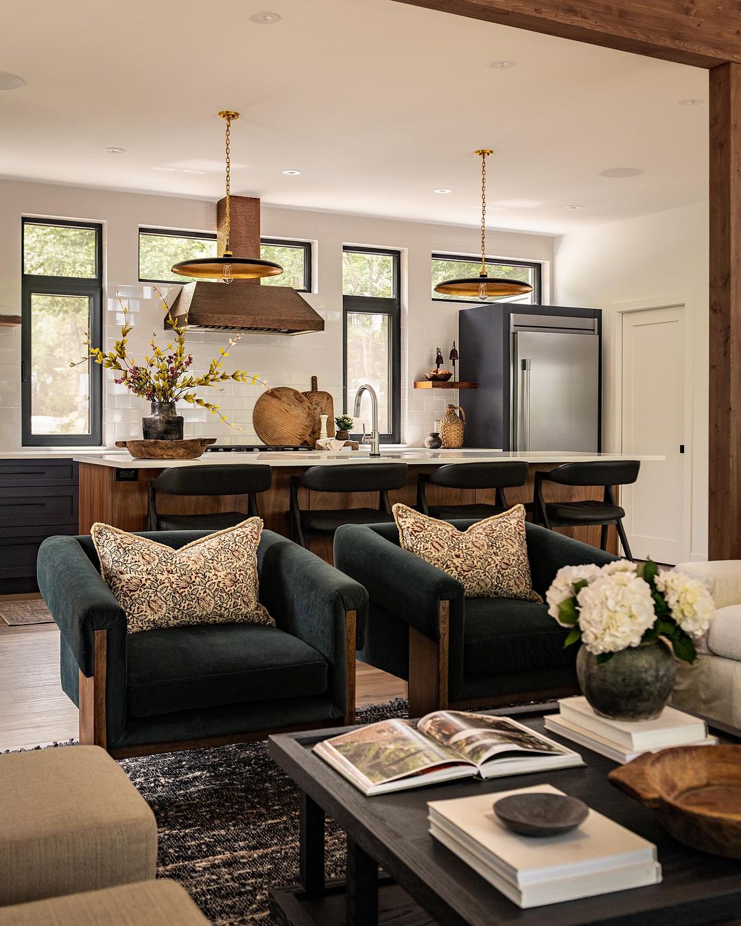 Modern and stylish open-concept living space featuring wooden beams and dark green accent chairs