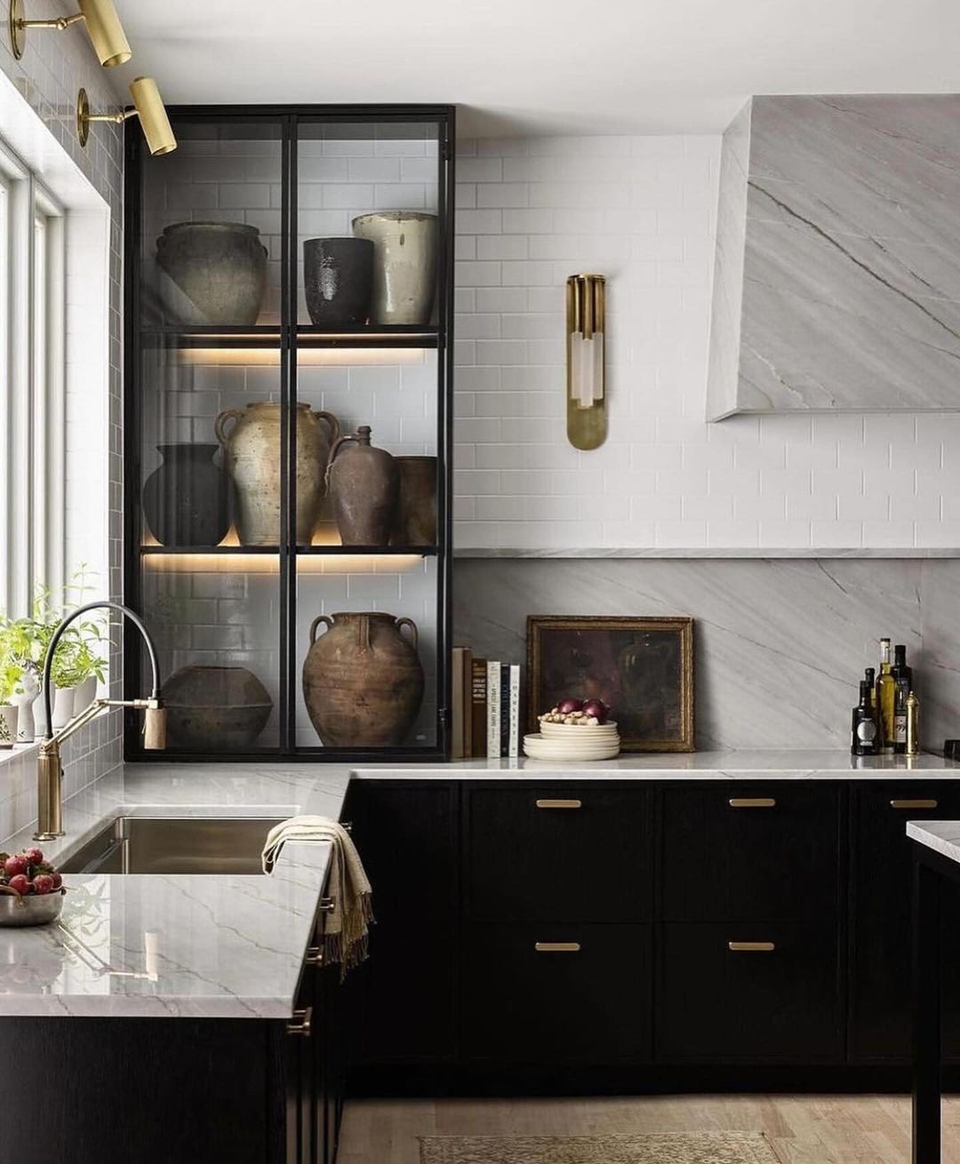 A sophisticated black and white kitchen featuring marble countertops, gold fixtures, and a display cabinet filled with vintage pottery.