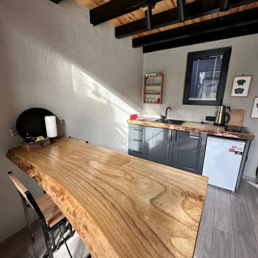 A modern kitchen featuring a large natural-edge wooden countertop, sleek gray cabinetry, and exposed wooden beams.