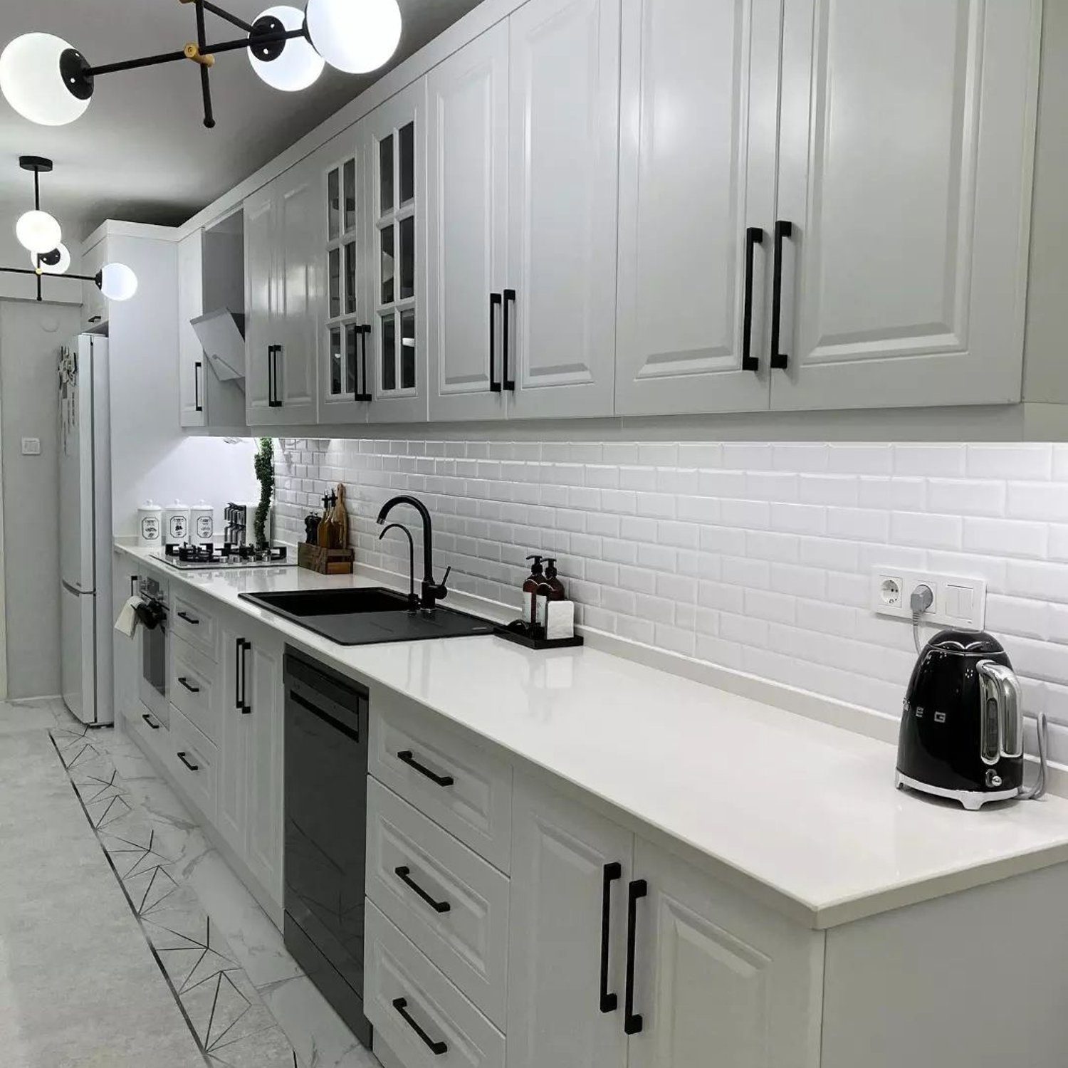 A modern kitchen with gray and white cabinetry, white subway tile backsplash, and black accents.