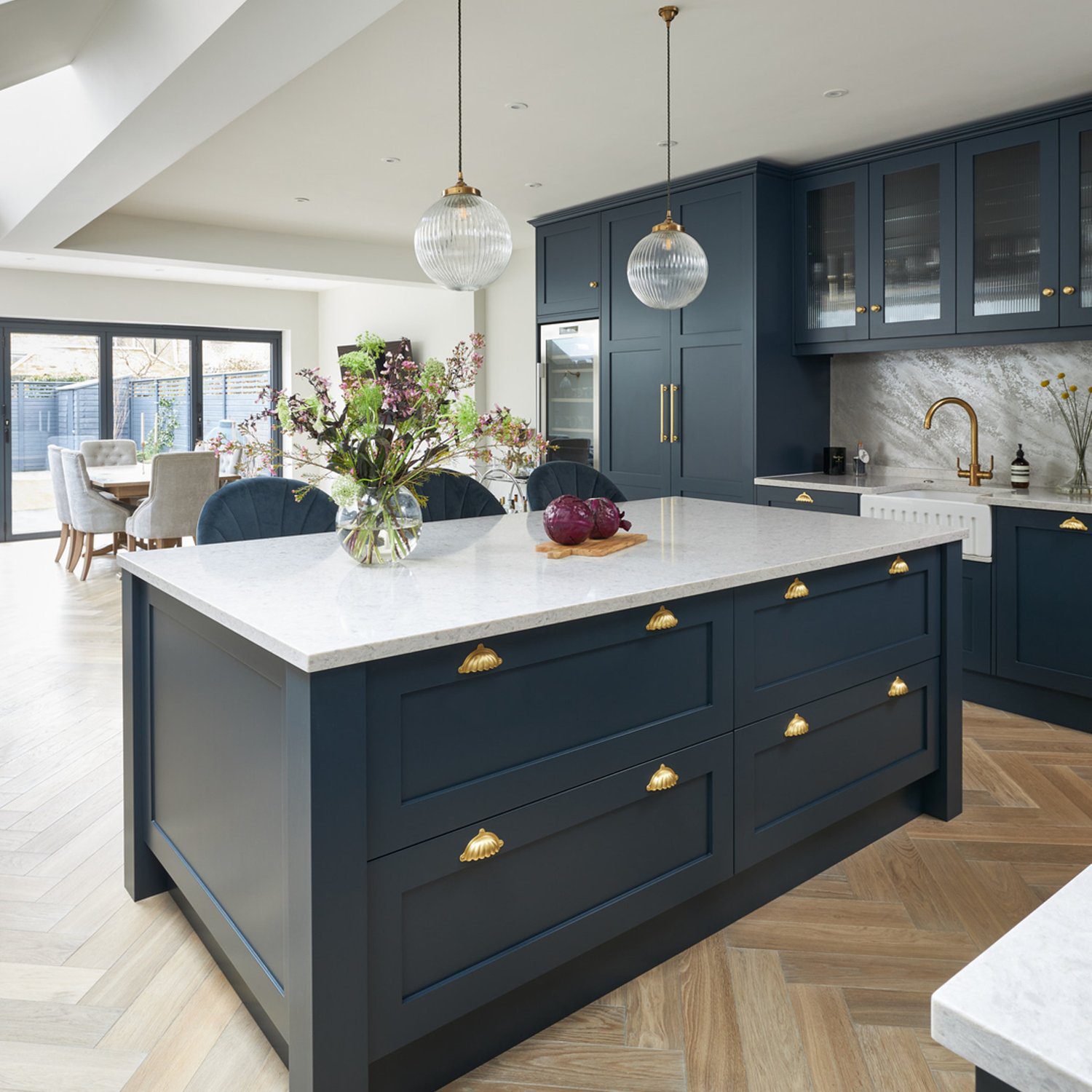 Elegant contemporary kitchen featuring deep blue cabinetry with brass accents, a large marble island, and herringbone wood flooring