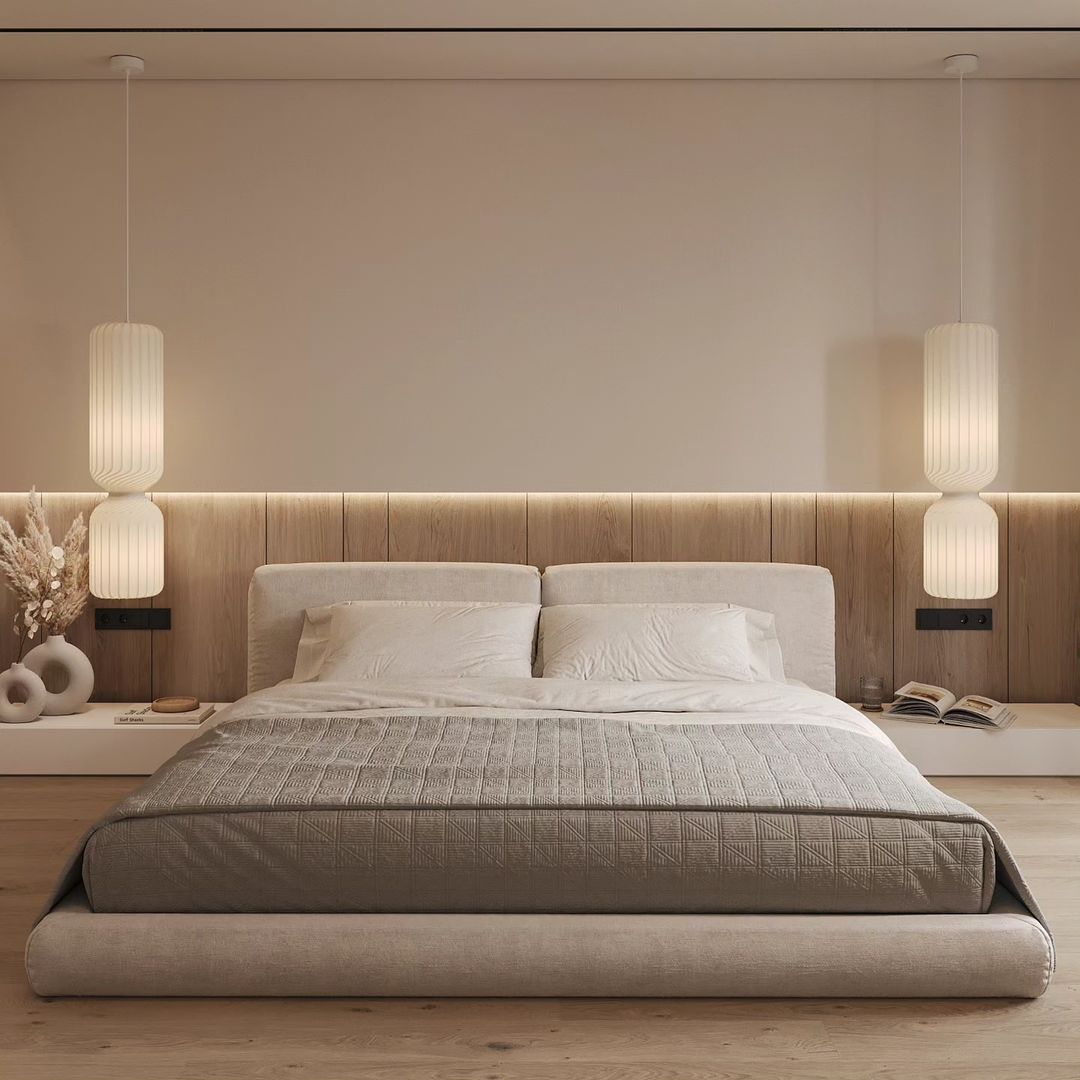 A minimalist bedroom design featuring a low-profile bed with neutral-toned linens, flanked by vertical hanging lamps and a wood-accented wall