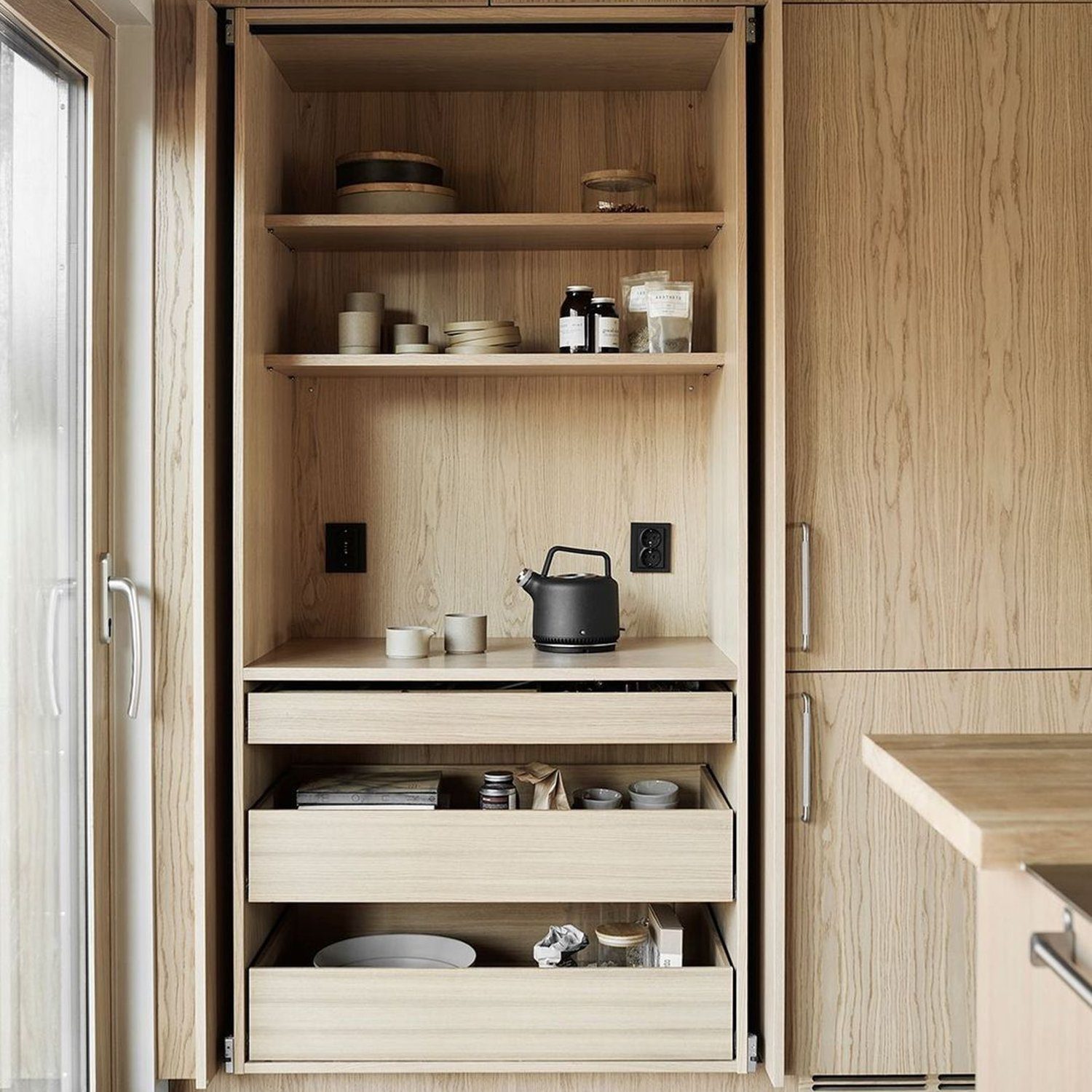 A sleek and modern kitchen pantry with open shelving featuring a variety of dishware and a black kettle